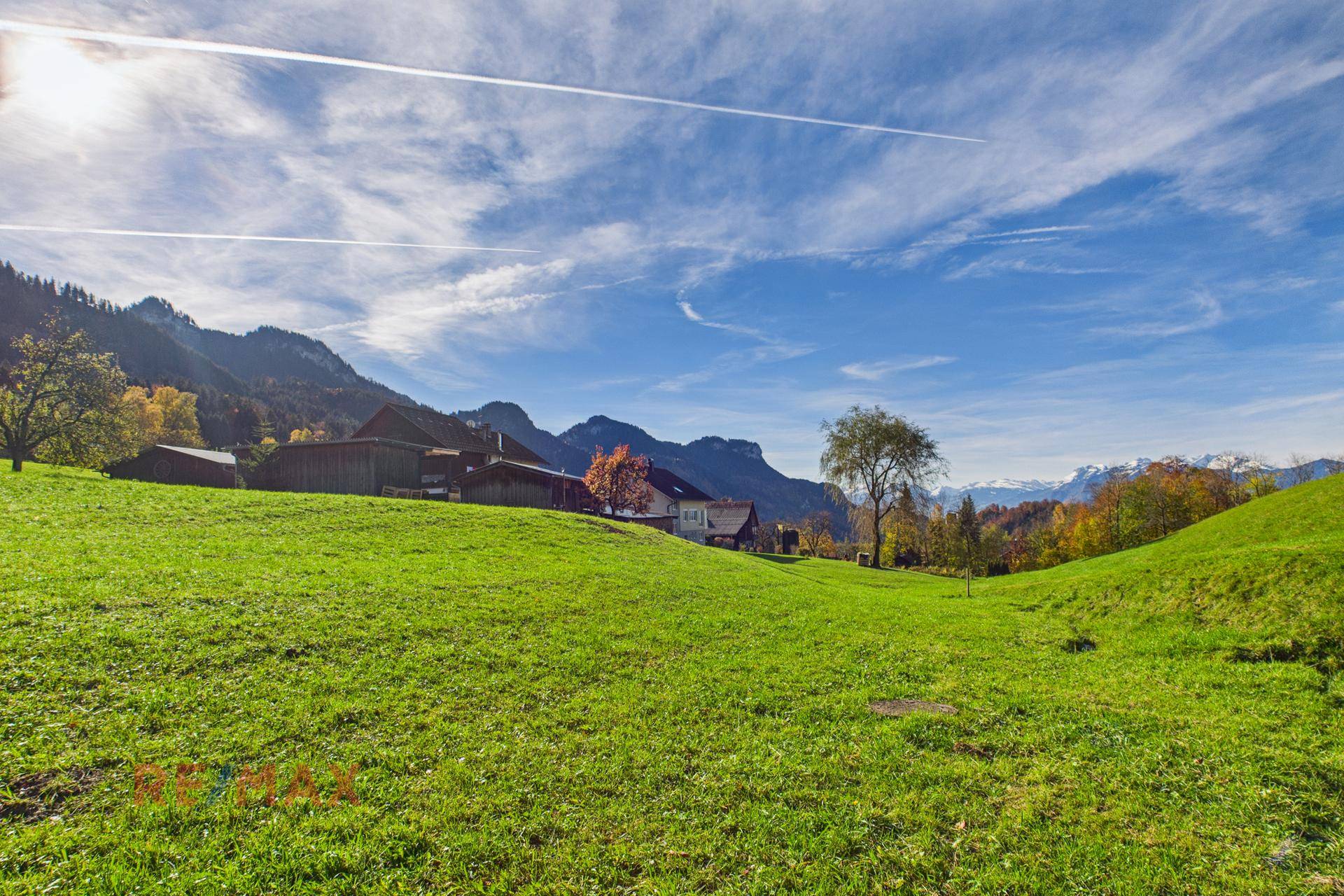 Weitläufige grüne Wiese mit Blick auf die umliegenden Berge und vereinzelte Häuser.