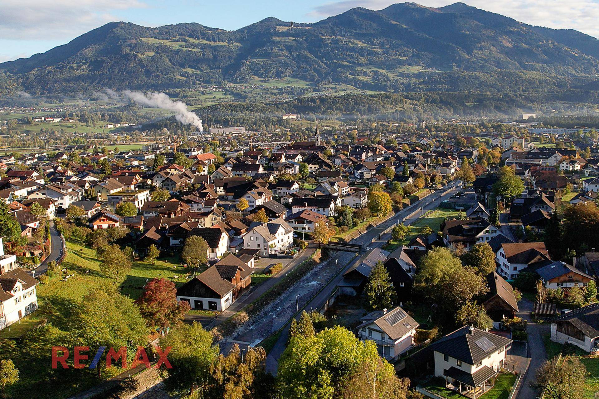 Weitläufige Luftaufnahme einer Wohngegend mit Bergen, Fluss und herbstlicher Vegetation.