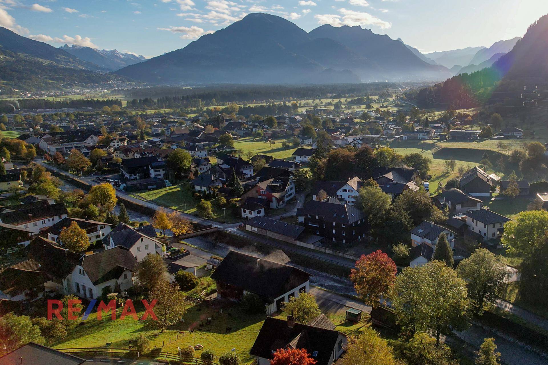 Luftbild der Wohnsiedlung in einer Berglandschaft mit herbstlichen Bäumen und Fluss.