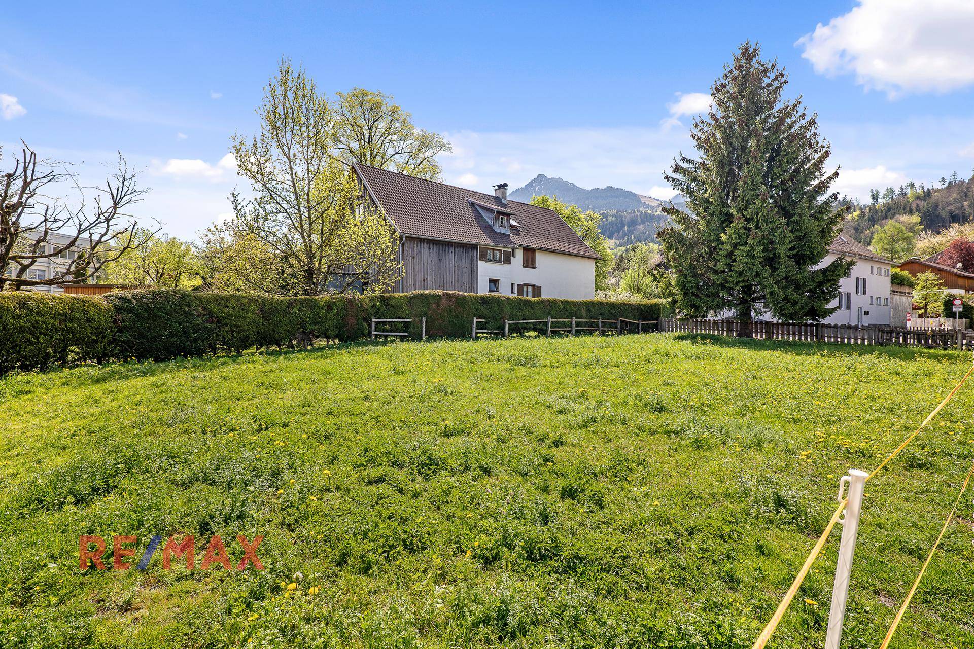 Weitläufige Grünfläche mit Blick auf ein traditionelles Haus und die umliegenden Berge.