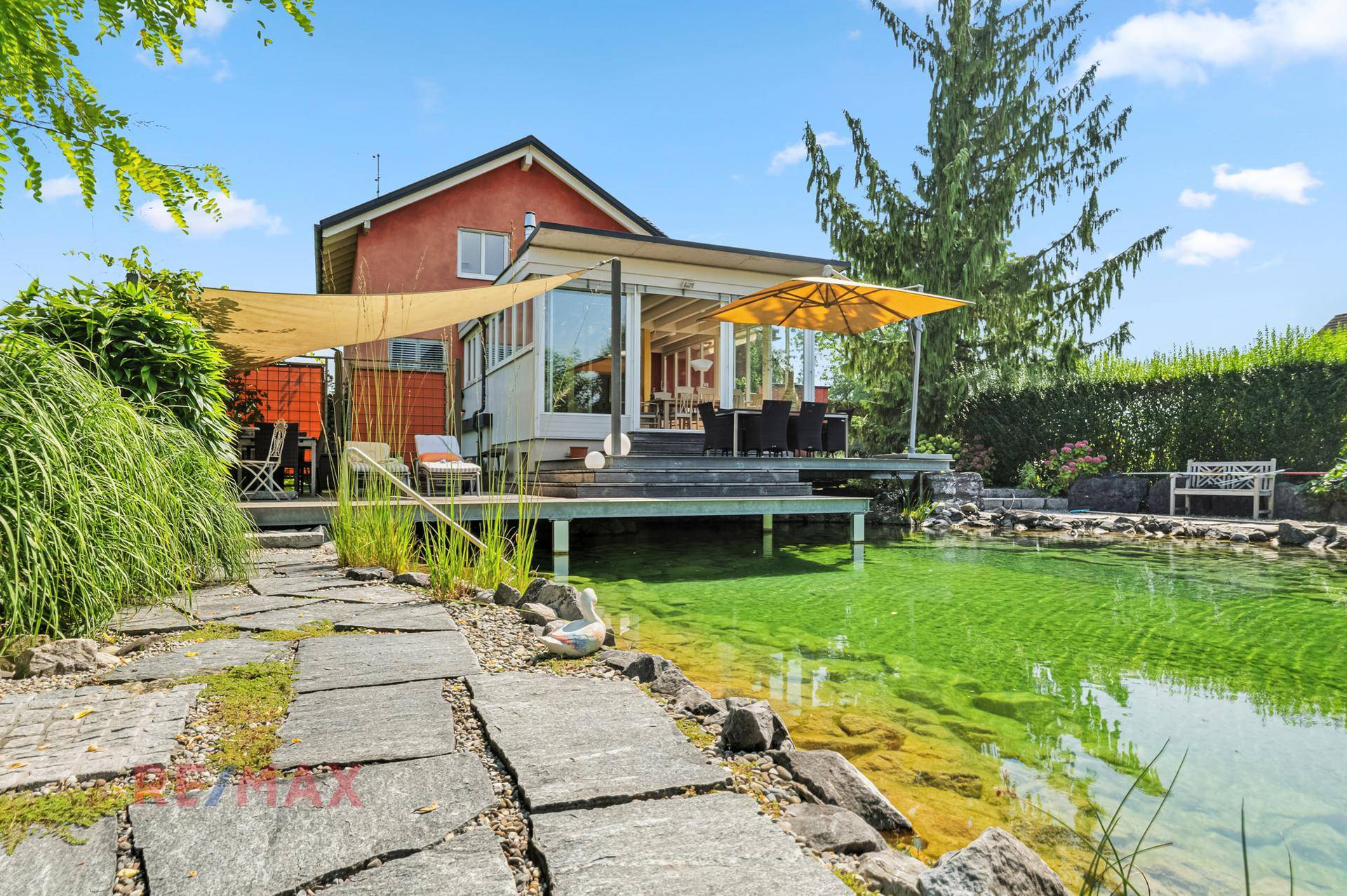 Steinplattenweg führt durch den gepflegten Garten zum Haus mit Terrasse und Naturschwimmteich.