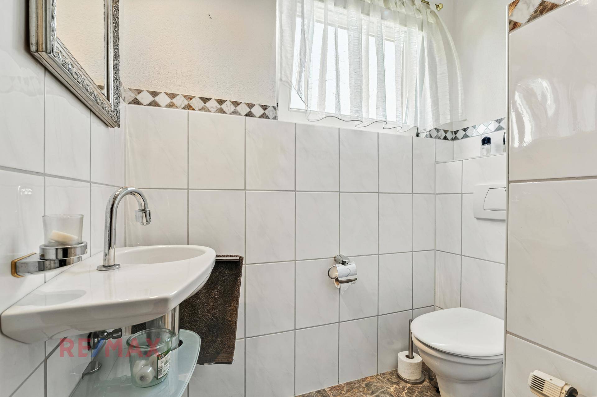 Helles Gäste-WC mit weißen Fliesen, modernem Waschbecken und Fenster.