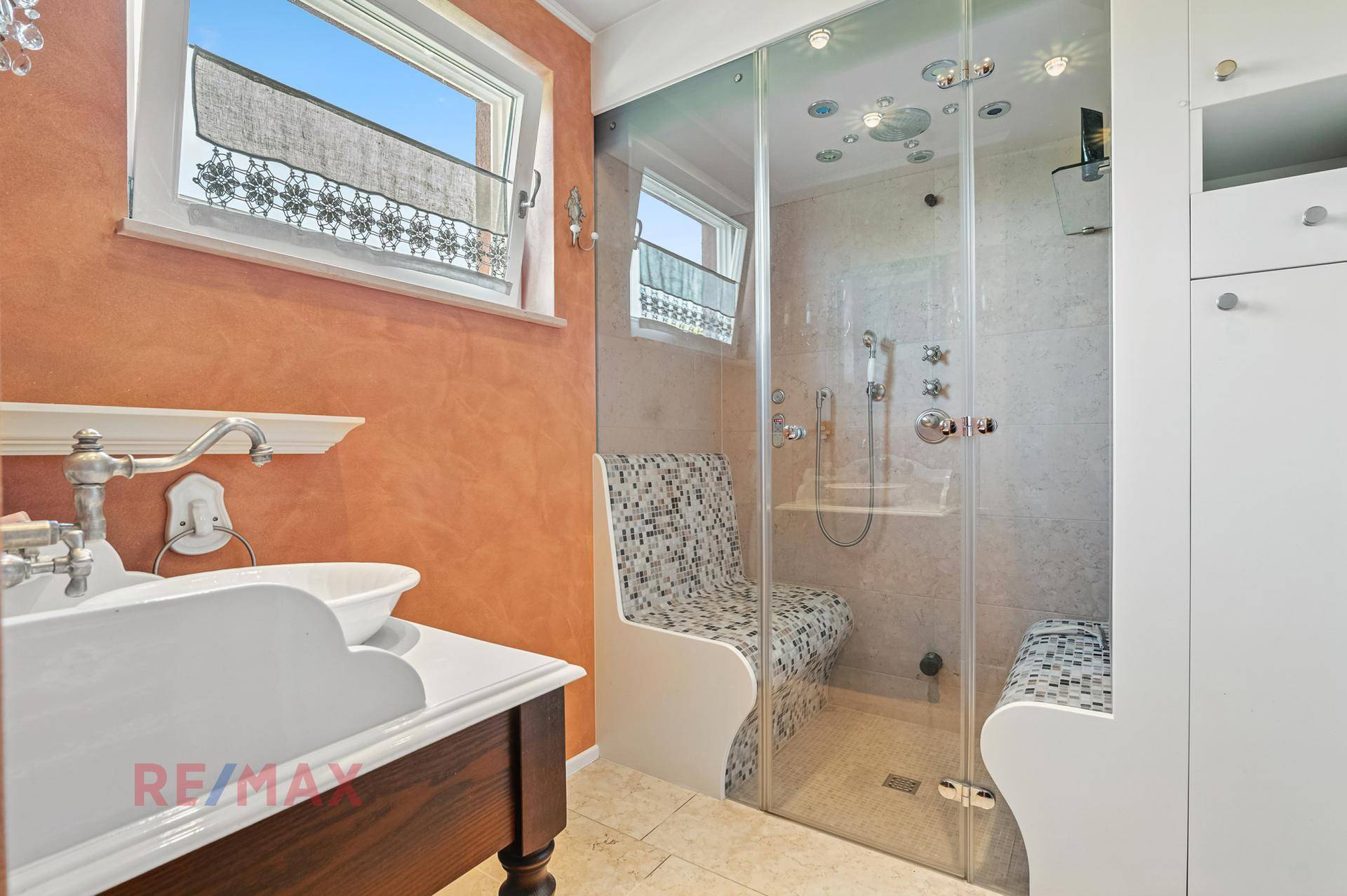 Modernes Badezimmer mit großer Duschkabine, Sitzgelegenheit und Fenster.