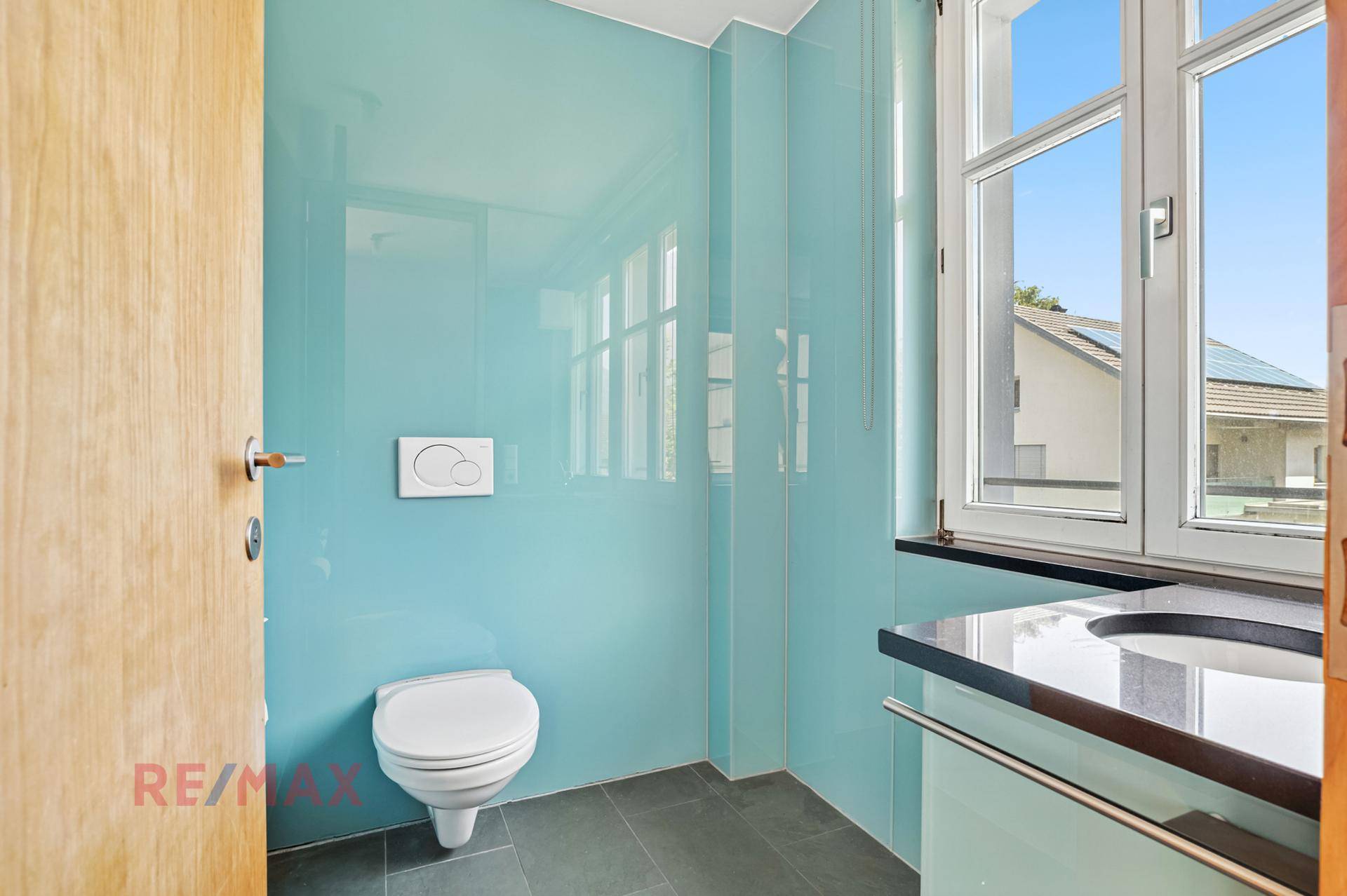 Modernes Gäste-WC mit blauen Glaswänden, Fenster und elegantem Waschtisch.