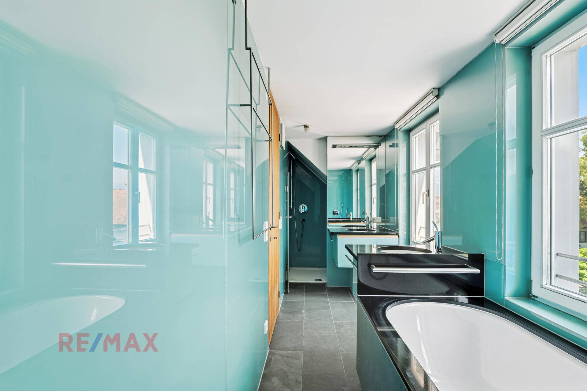 Geräumiges Badezimmer mit blauen Glaswänden, Badewanne, Dusche und Doppelwaschbecken.