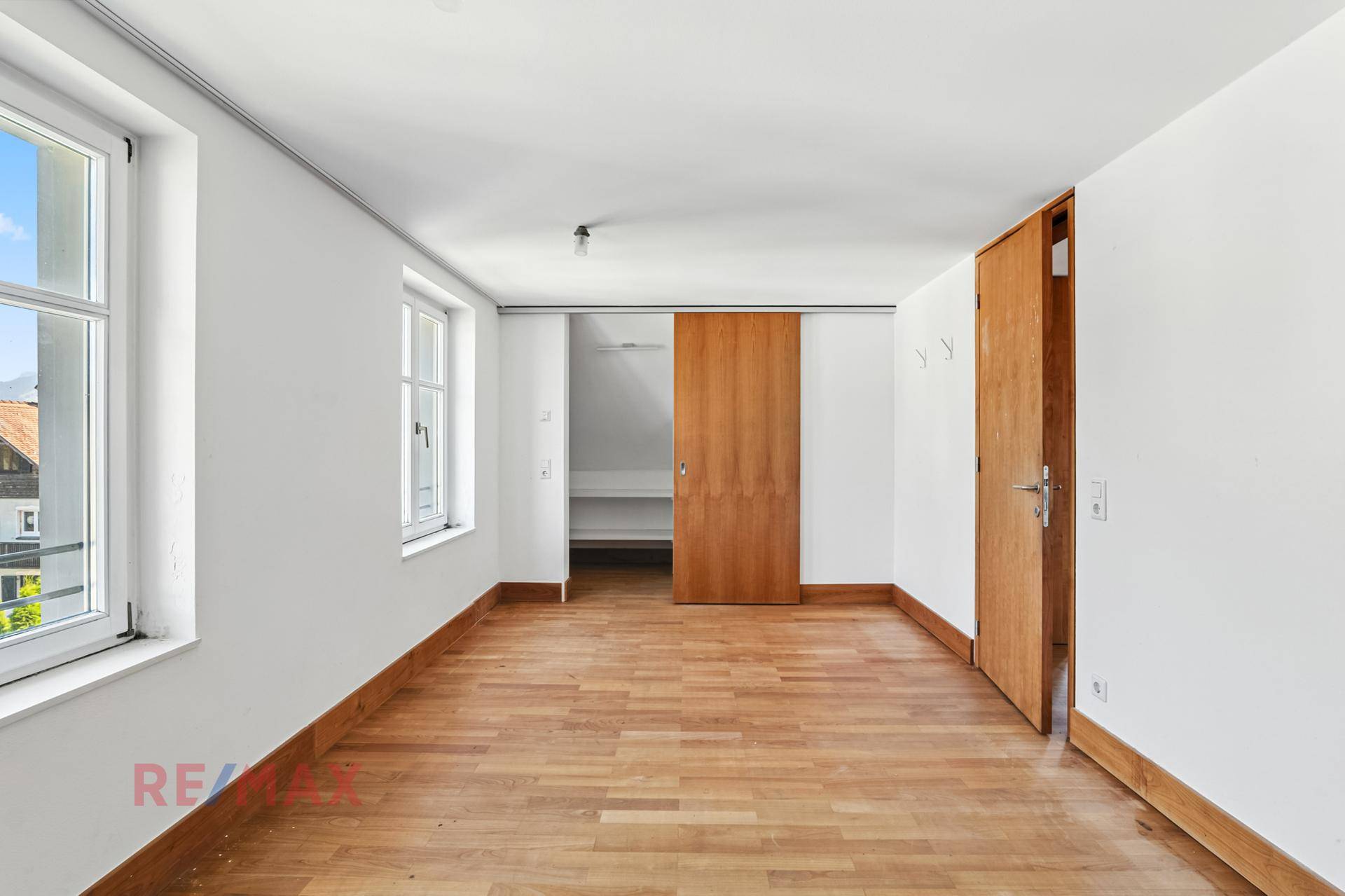 Helles Schlafzimmer mit Holzboden und Schiebetür zu einem begehbaren Kleiderschrank.