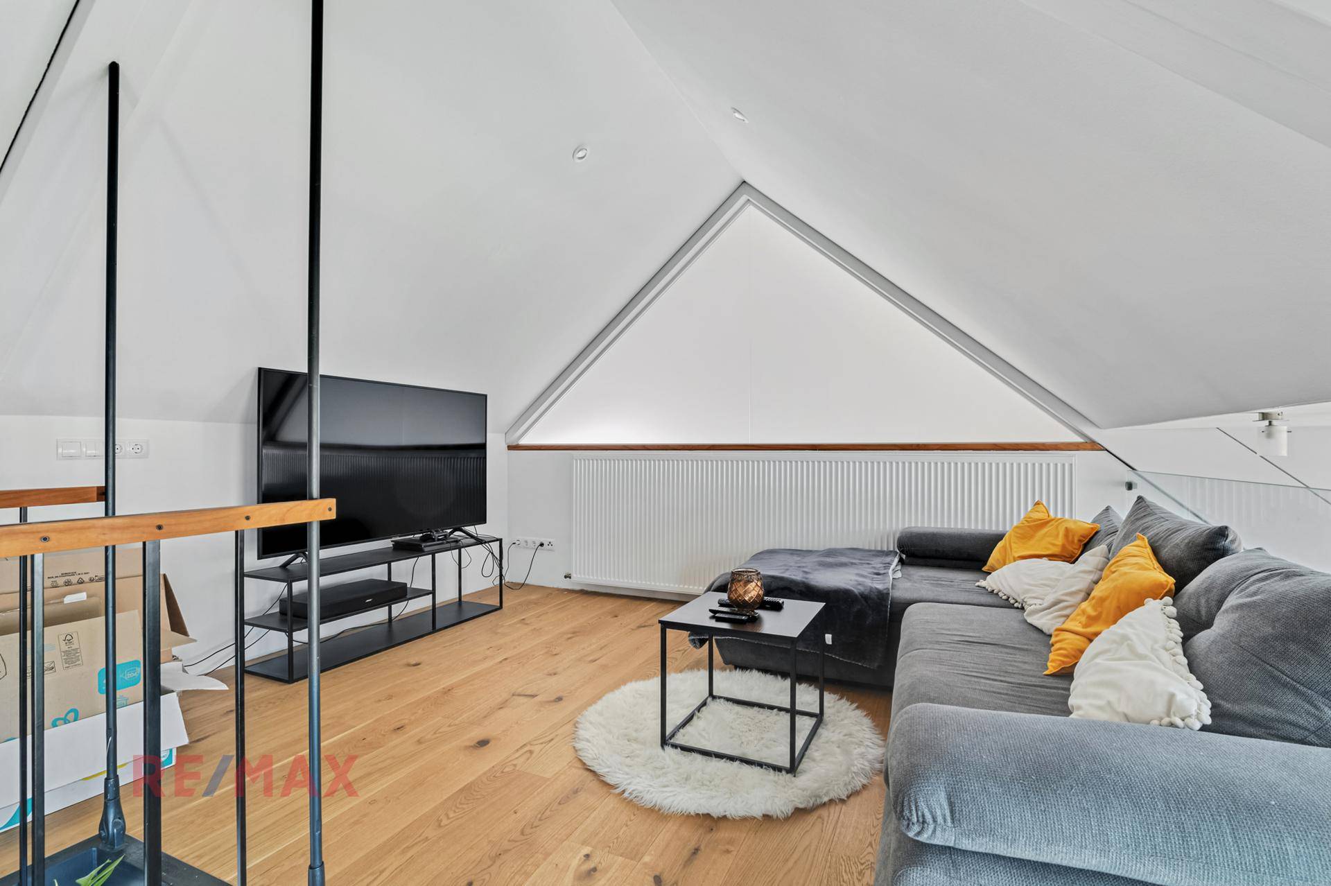 Gemütlicher Wohnbereich im Dachgeschoss mit Sofa, Fernseher und Holzboden unter schrägen Decken.