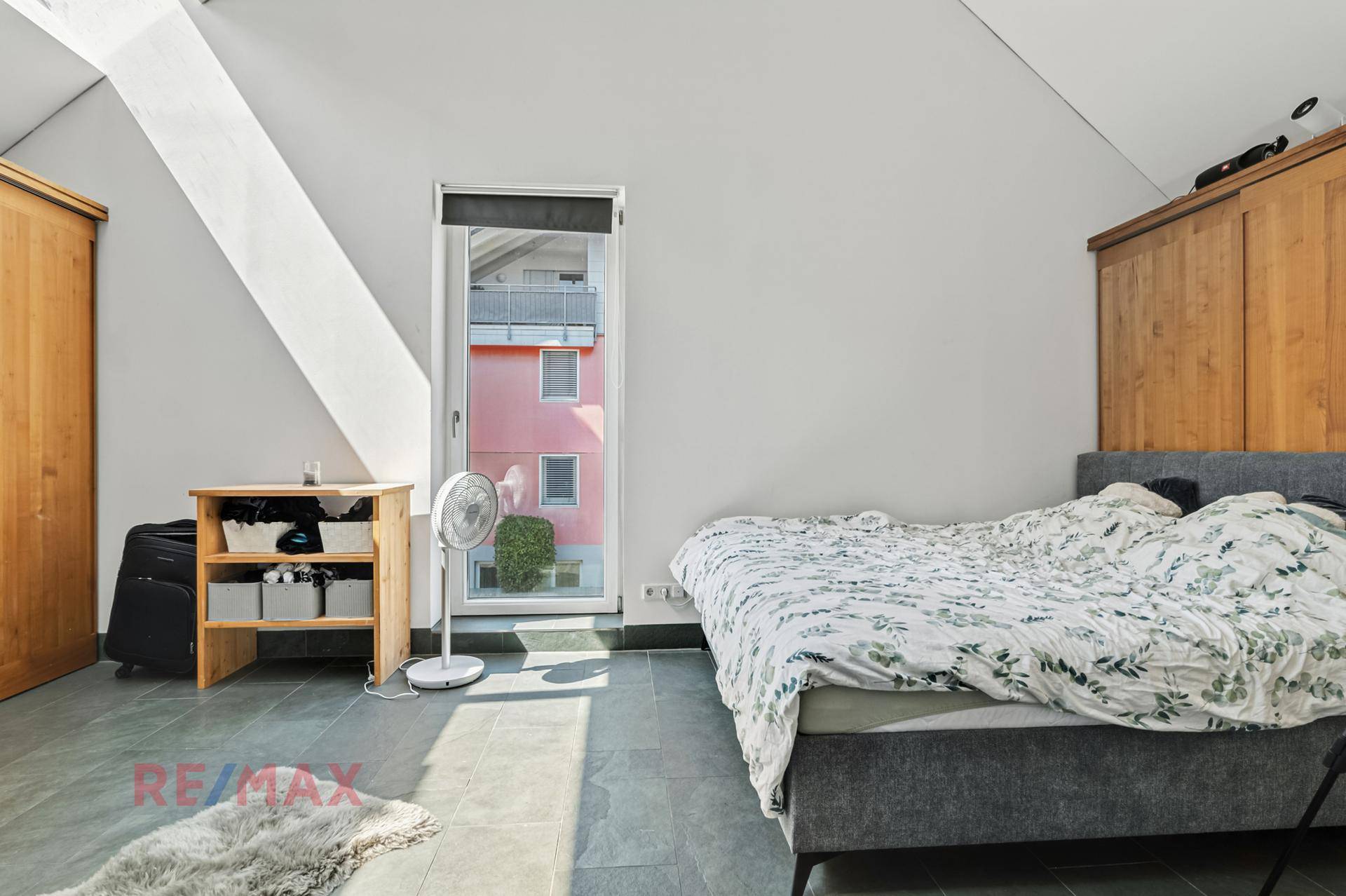 Schlafzimmer mit Doppelbett, Steinfliesenboden und Zugang zu einem Balkon, der viel Licht bietet.