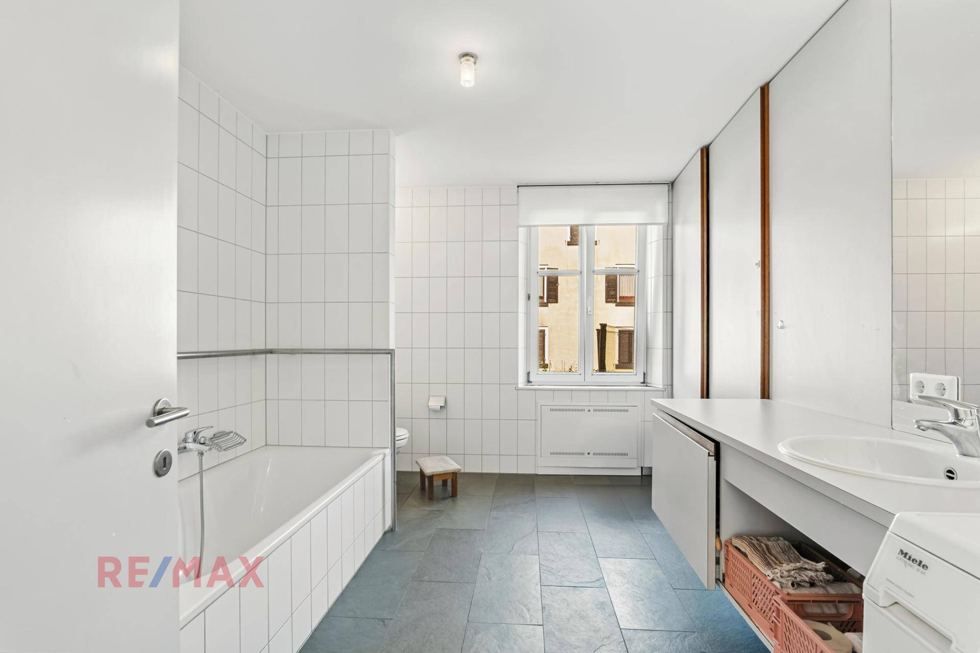 Helles Badezimmer mit Badewanne, weißen Fliesen und Fenster, das viel Tageslicht hereinlässt.
