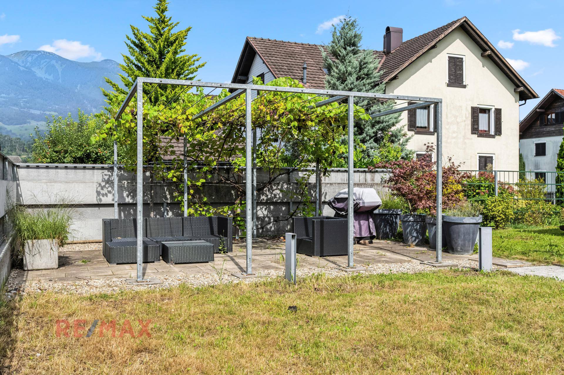 Sonniger Garten mit Pergola, Grillplatz und Bergblick, der zum Verweilen einlädt.