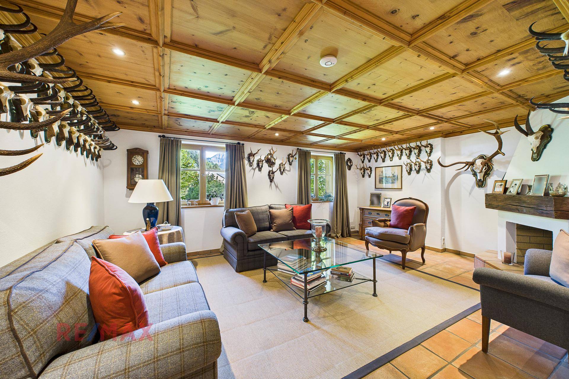 Geräumiges Wohnzimmer im alpinen Stil mit Holzkassettendecke, Kamin und Jagdtrophäen.