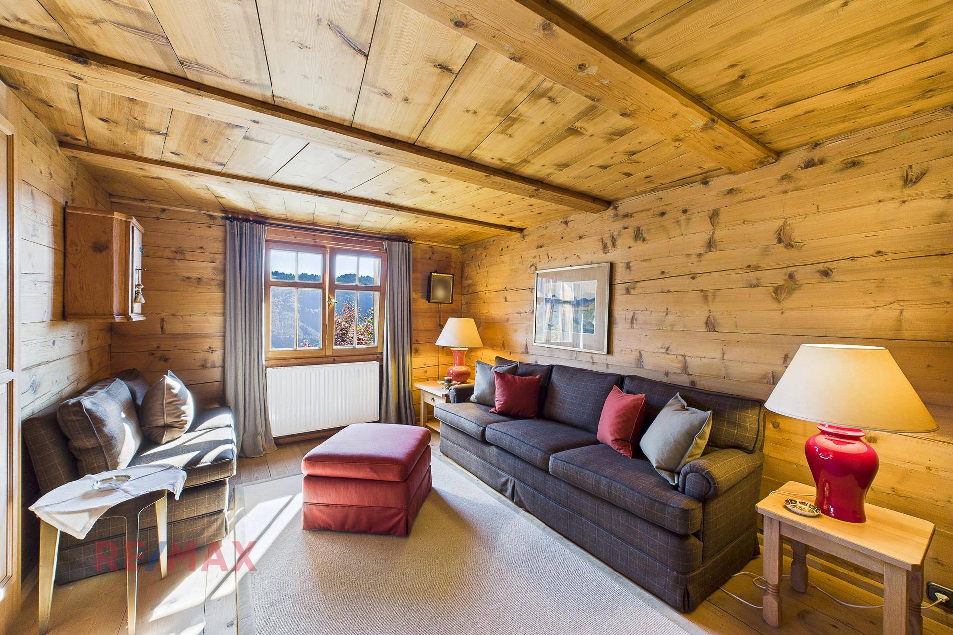 Gemütliches Wohnzimmer mit Holzwänden, Holzbalkendecke und bequemen Sitzmöbeln.