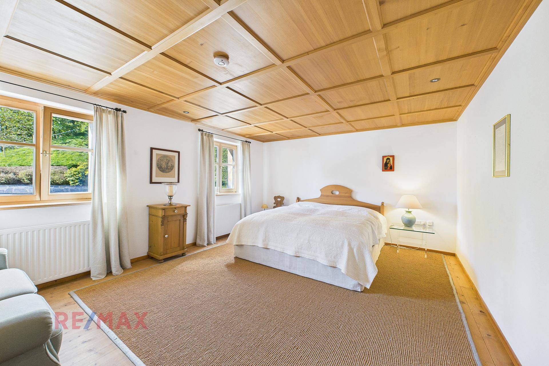 Geräumiges Schlafzimmer mit Holzkassettendecke, Teppichboden und Blick ins Grüne.