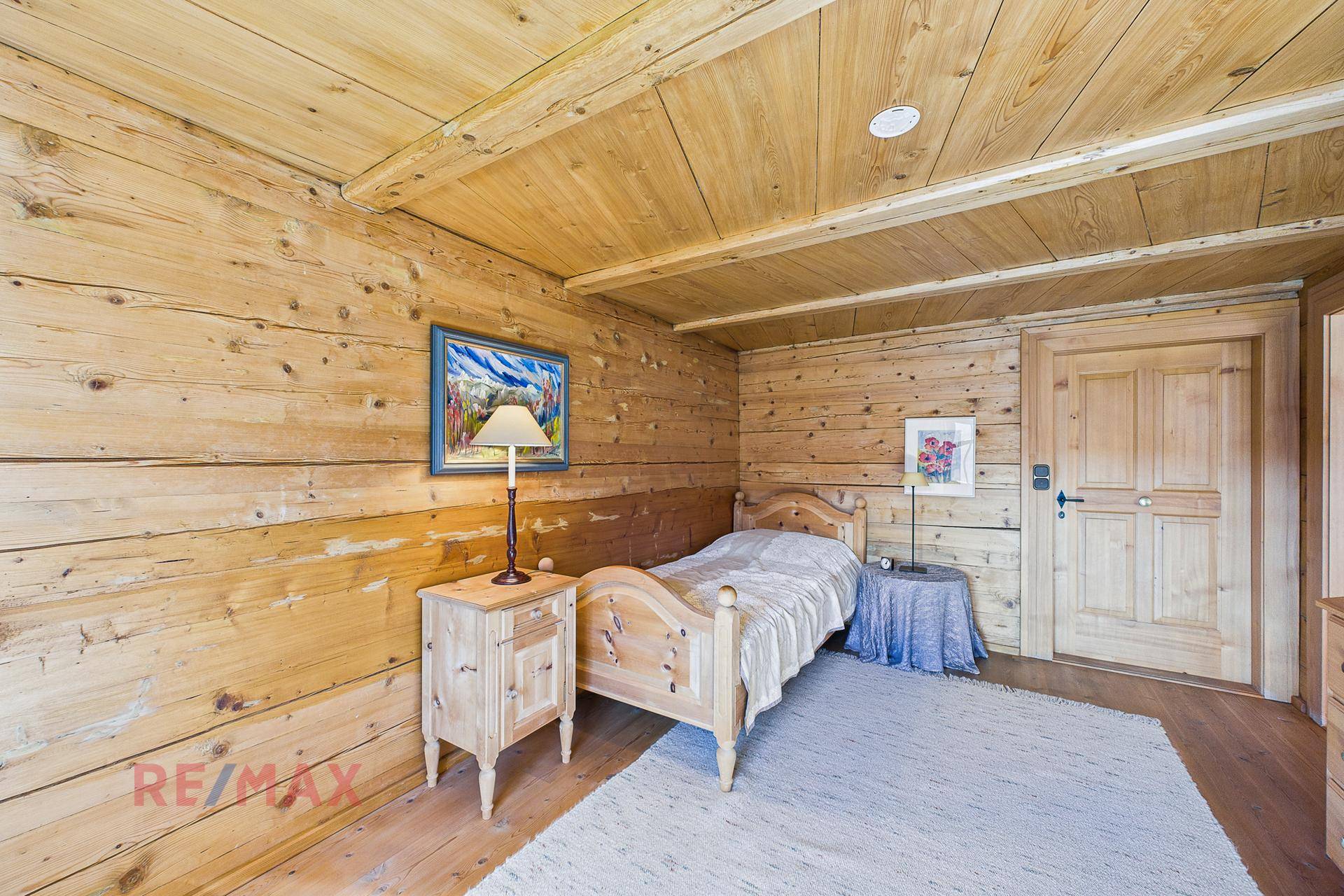 Kleines Schlafzimmer mit Holzwänden, Holzbalkendecke und Einzelbett im Landhausstil.