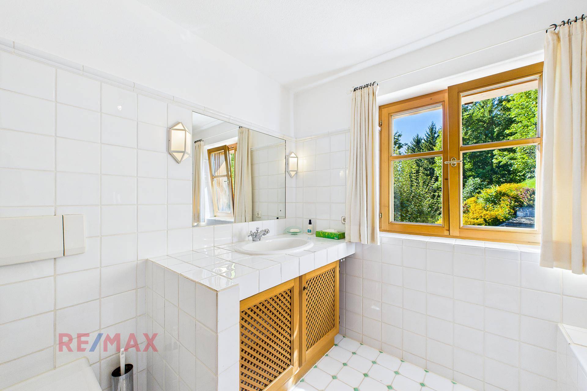 Helles Badezimmer mit Fenster, weißen Fliesen und traditionellem Waschtisch.