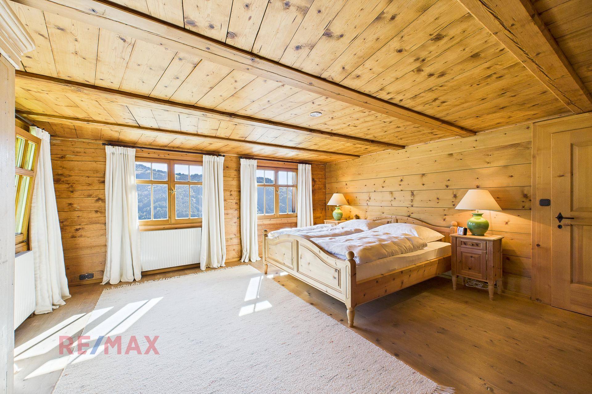 Großes Schlafzimmer mit Holzwänden, Holzbalkendecke und Teppichboden.