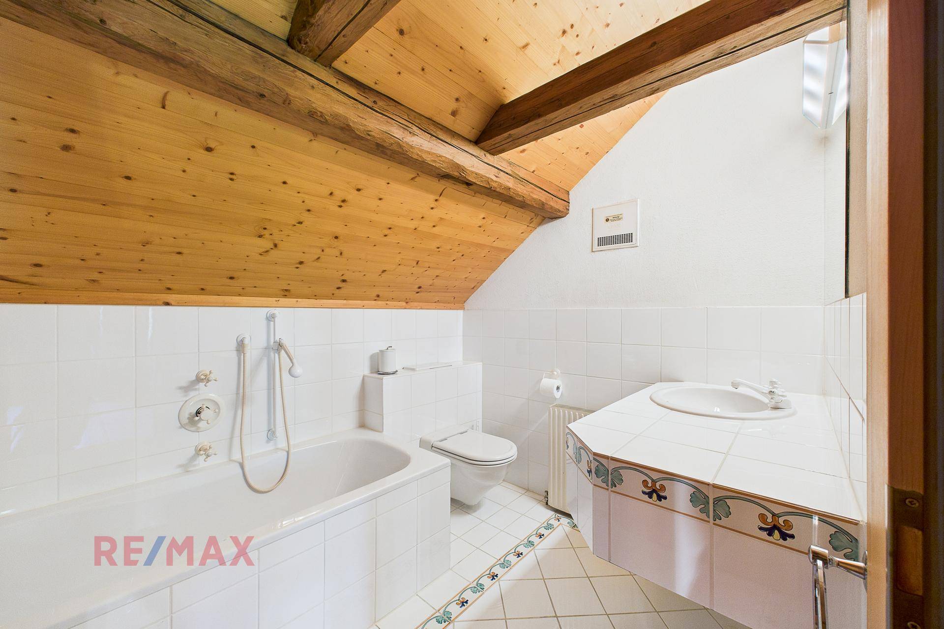 Helles Badezimmer im Dachgeschoss mit Badewanne, weißen Fliesen und Dachschräge.