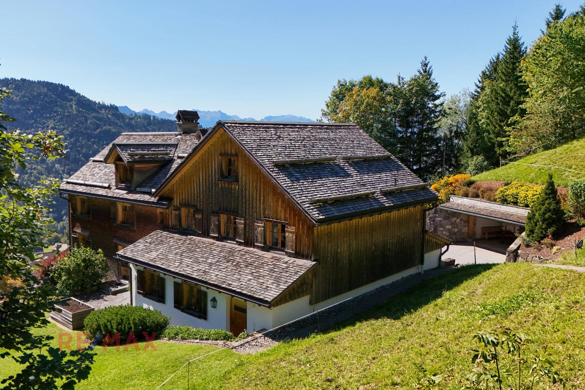 Seitenansicht des Holzhauses mit weitläufiger Grünfläche und Bergblick.