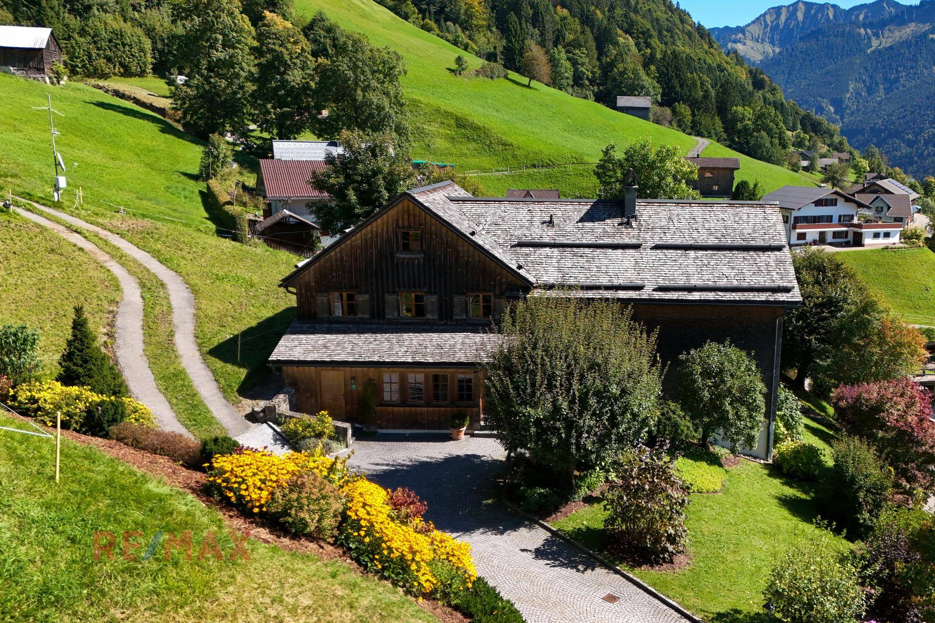 Gesamtansicht des Anwesens mit farbenfrohen Blumenbeeten und weitläufiger Grünfläche.