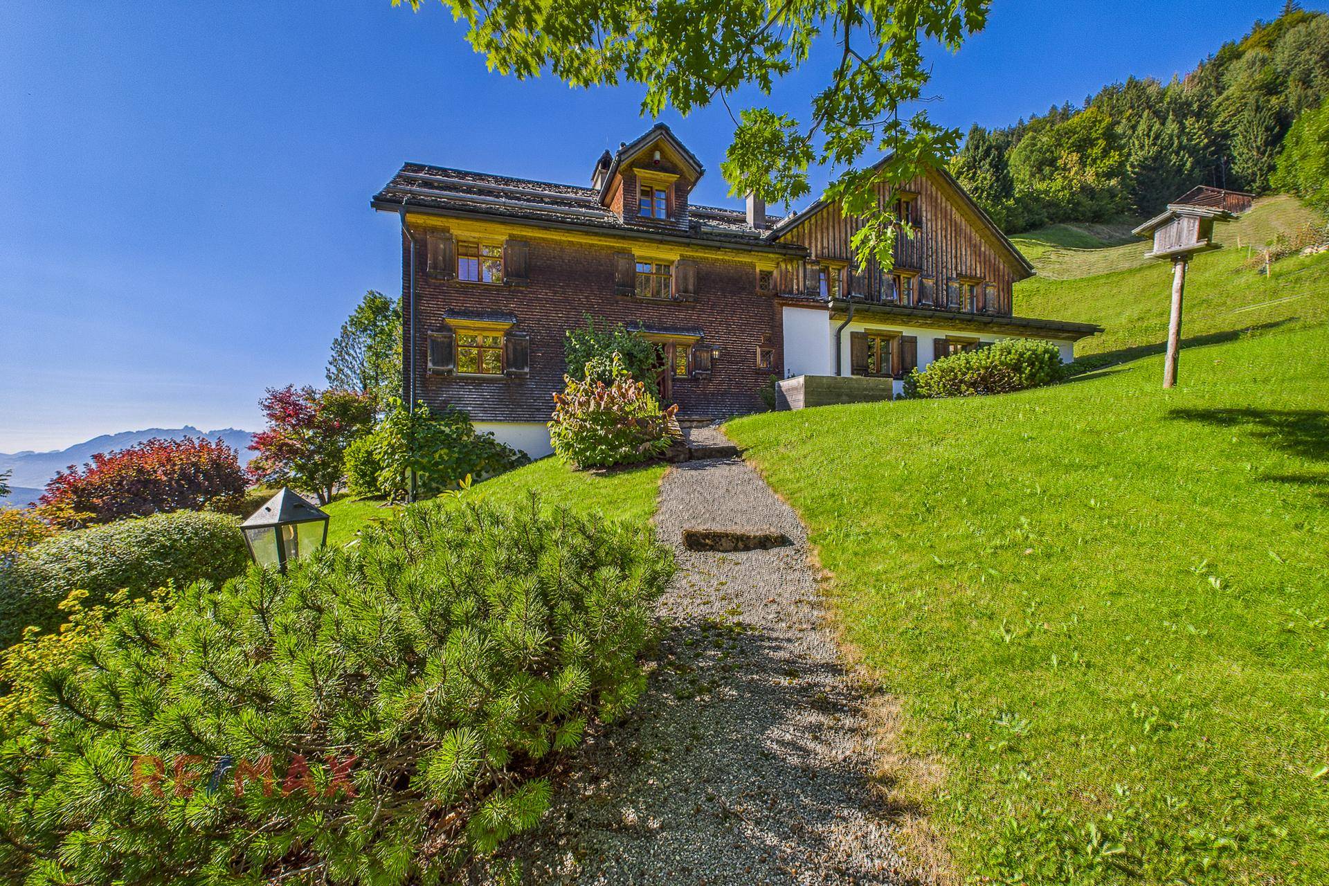 Idyllischer Gartenweg führt zum Haus, umgeben von üppigem Grün und Bergblick.