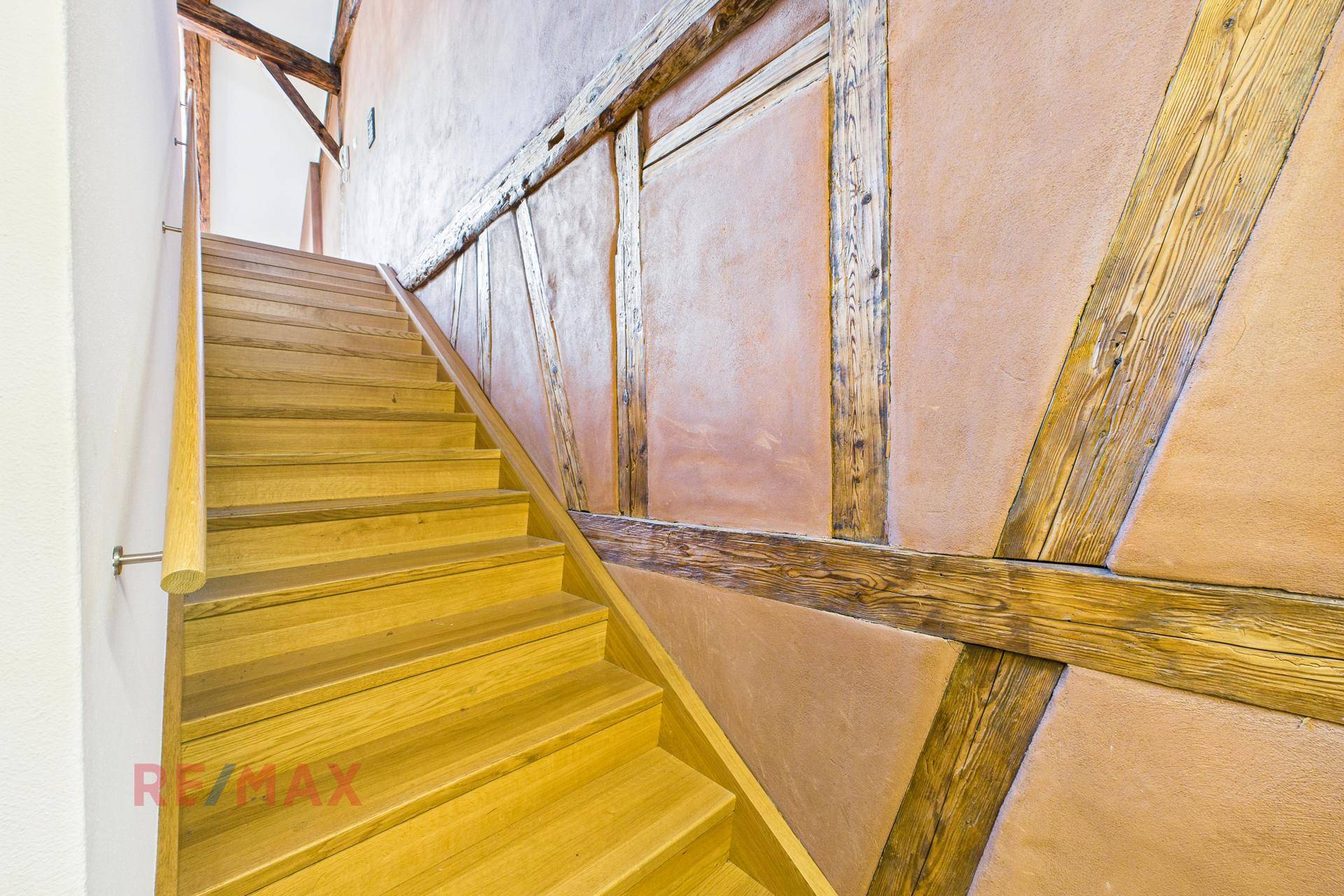 Holztreppe mit rustikalen Holzbalken und einer Wandverkleidung in warmem Erdton, die zum Dachgeschoss führt.