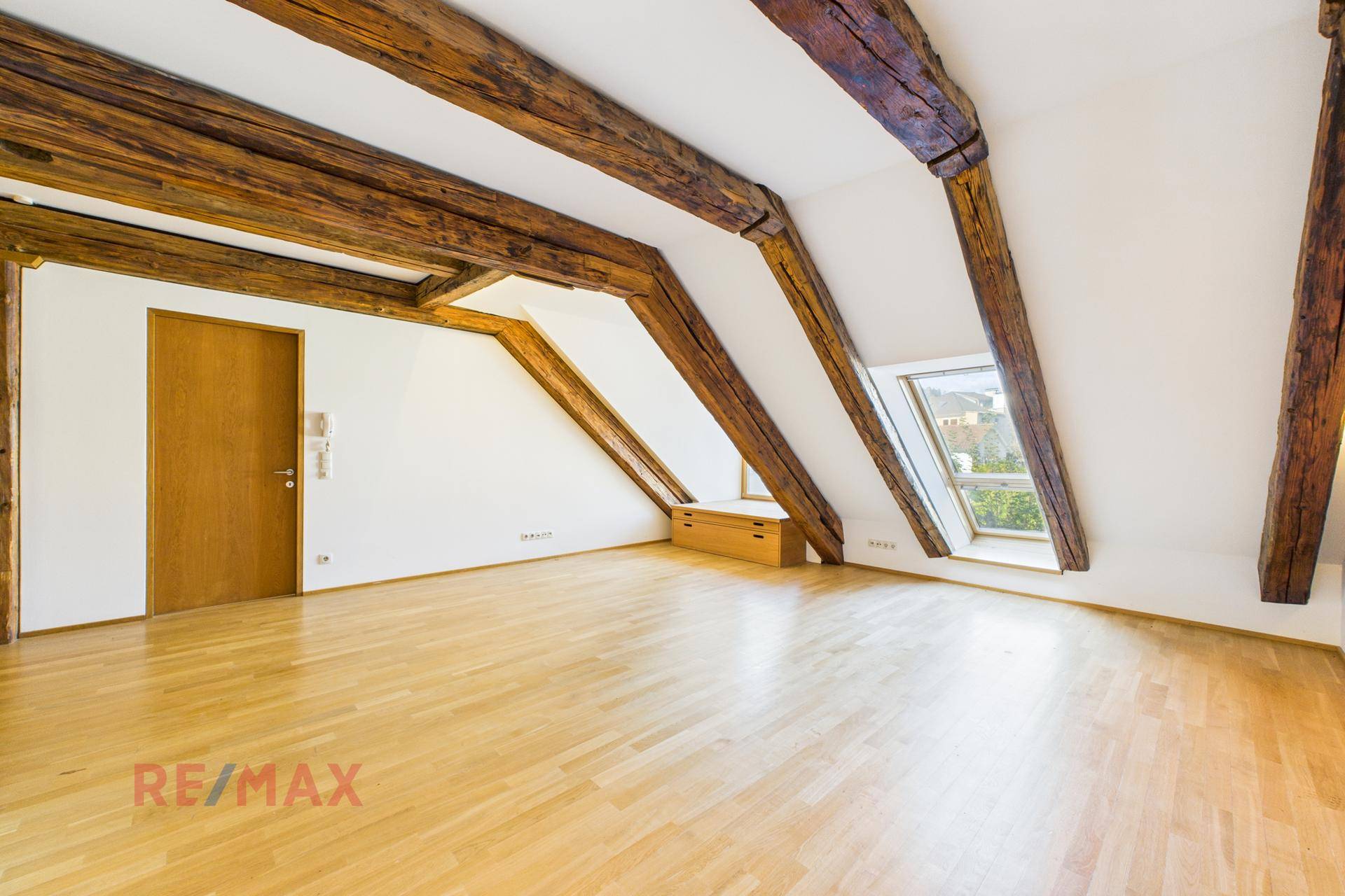 Helles Zimmer im Dachgeschoss mit Holzbalken, Dachfenstern und hellem Parkettboden, ideal als Schlafzimmer.