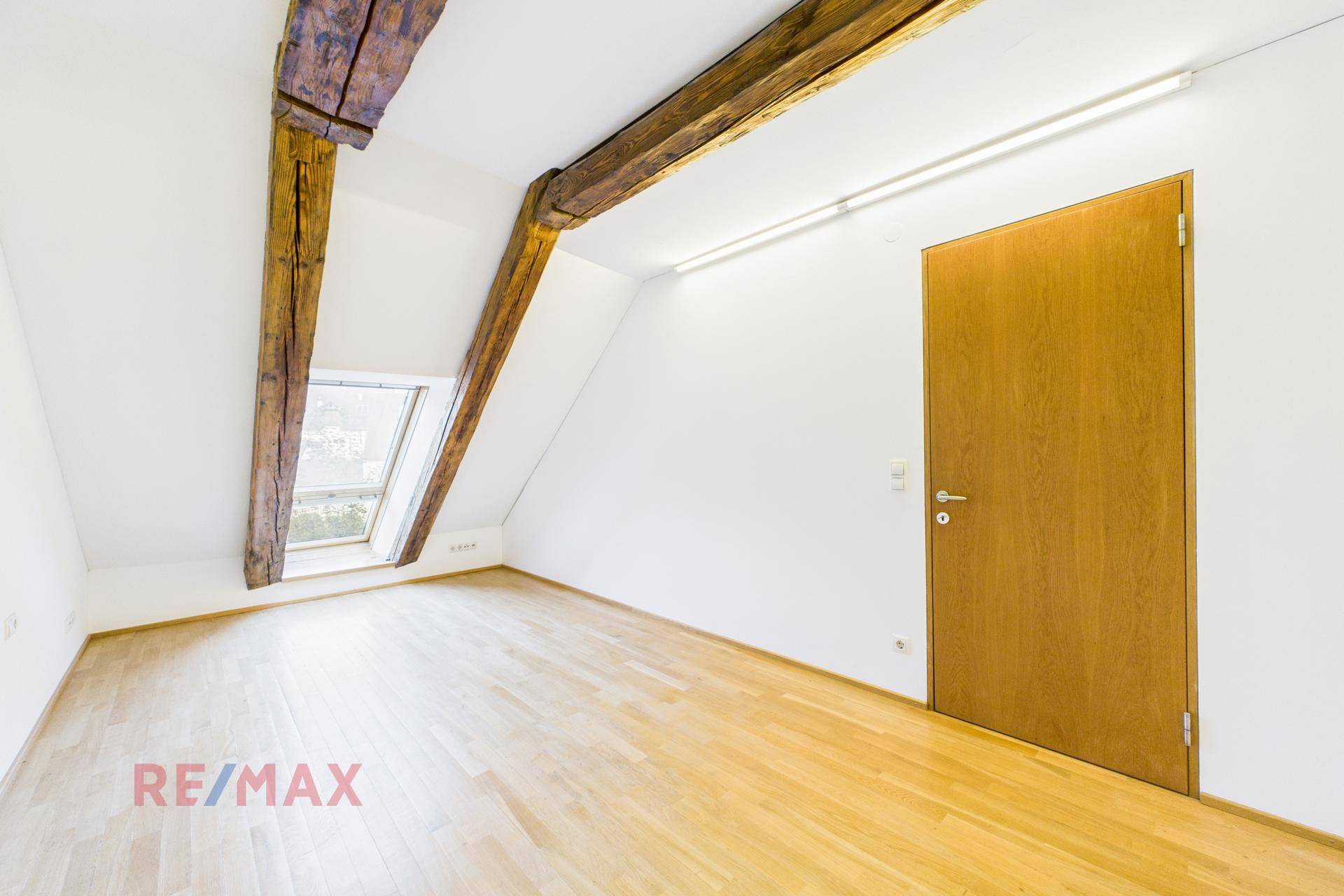 Geräumiges Zimmer im Dachgeschoss mit Holzbalken, Dachfenster und hellem Parkettboden, gut beleuchtet.