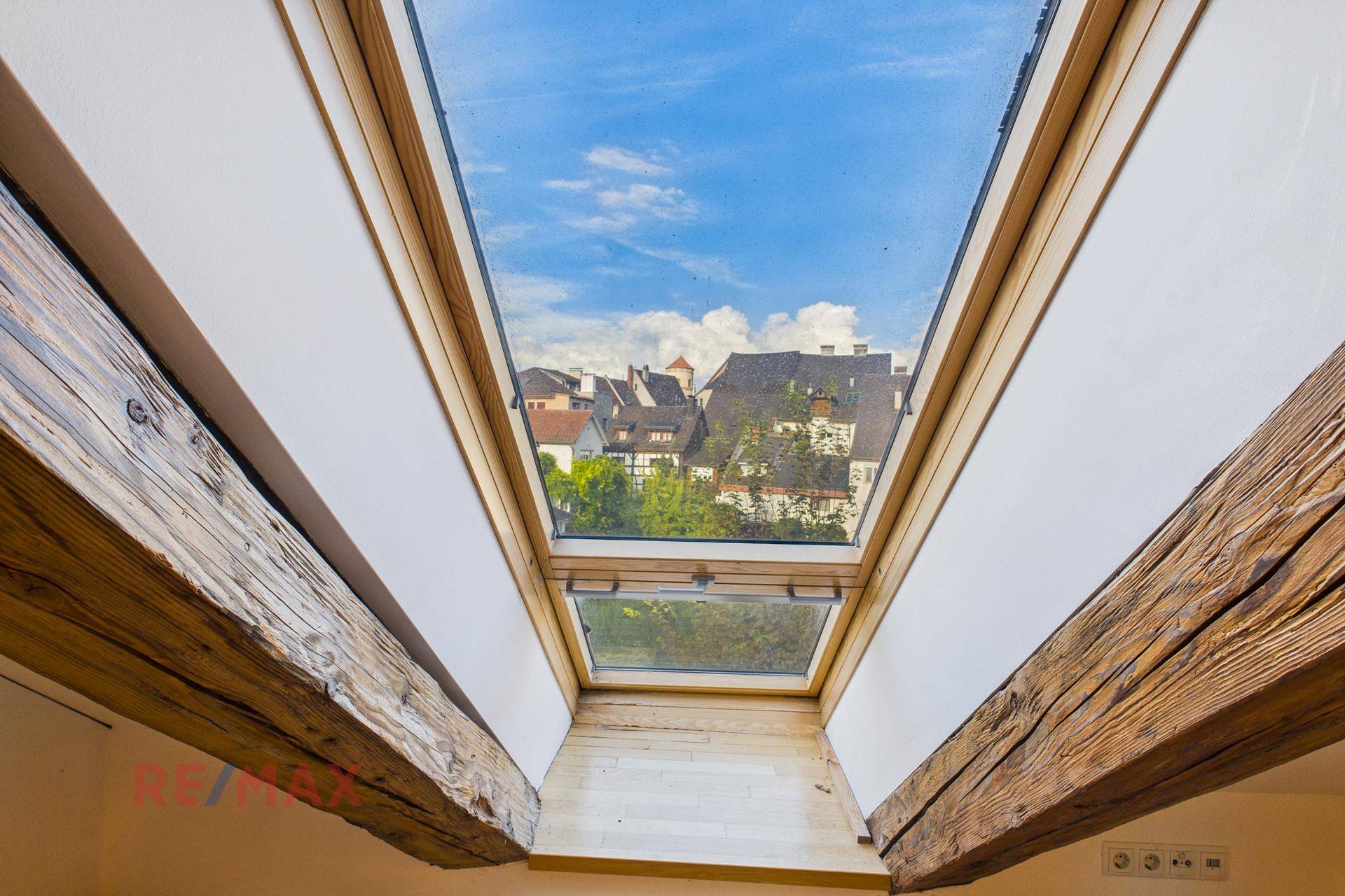 Dachfenster mit Blick auf die Dächer der Altstadt und den blauen Himmel, das viel Licht hereinlässt.