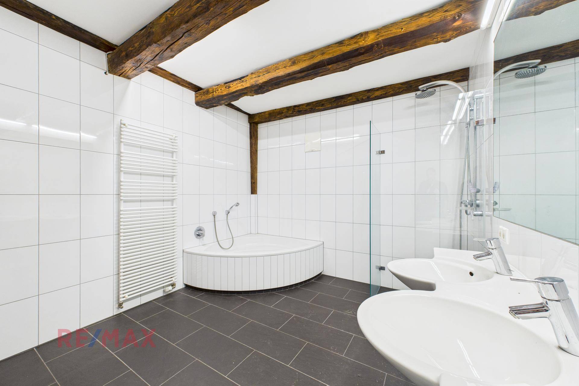 Modernes Badezimmer mit weißen Fliesen, dunklem Fliesenboden, Eckbadewanne und separater Dusche.
