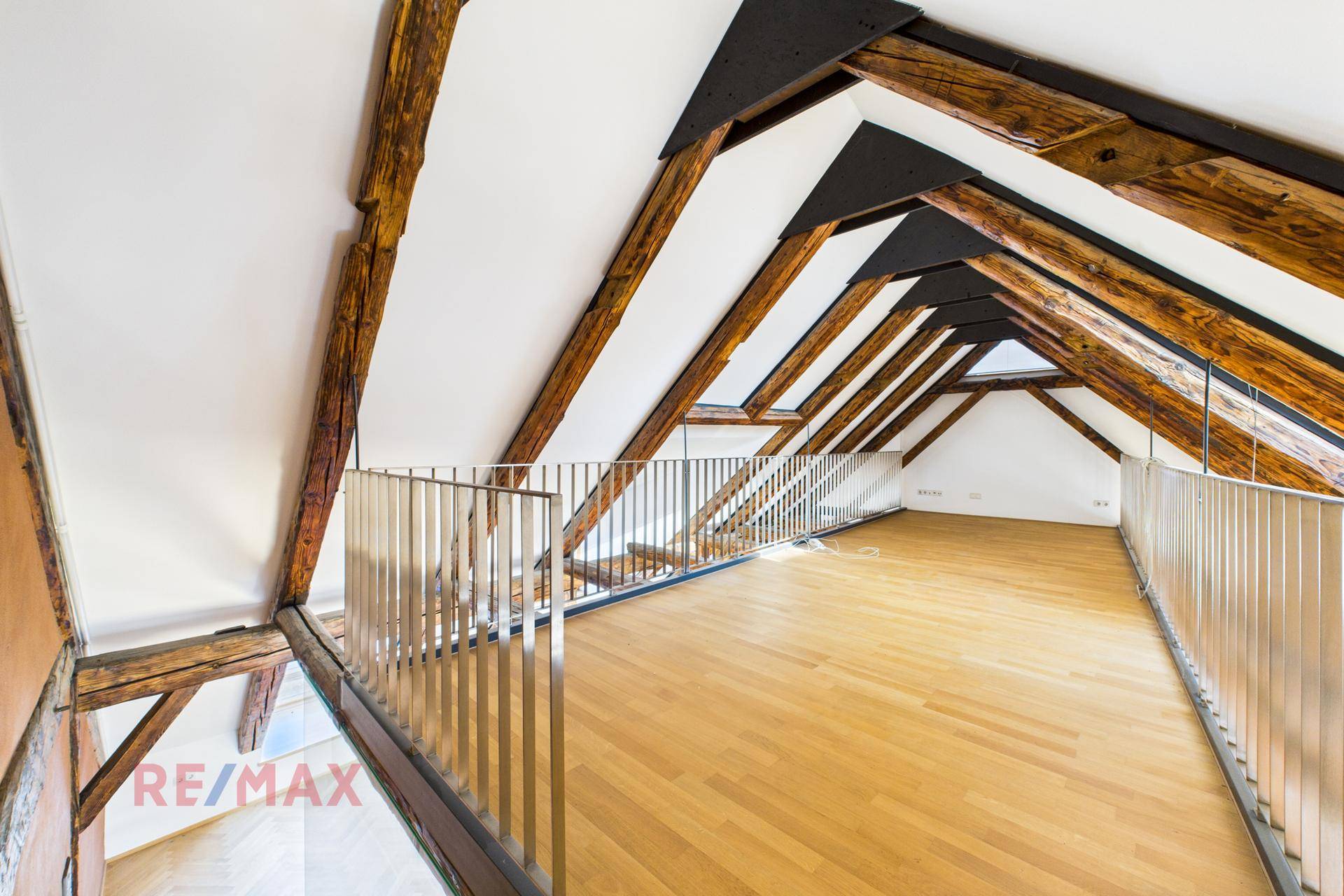 Geräumige Galerie im Dachgeschoss mit Holzbalken, hellem Parkettboden und Metallgeländer, das den Raum abgrenzt.