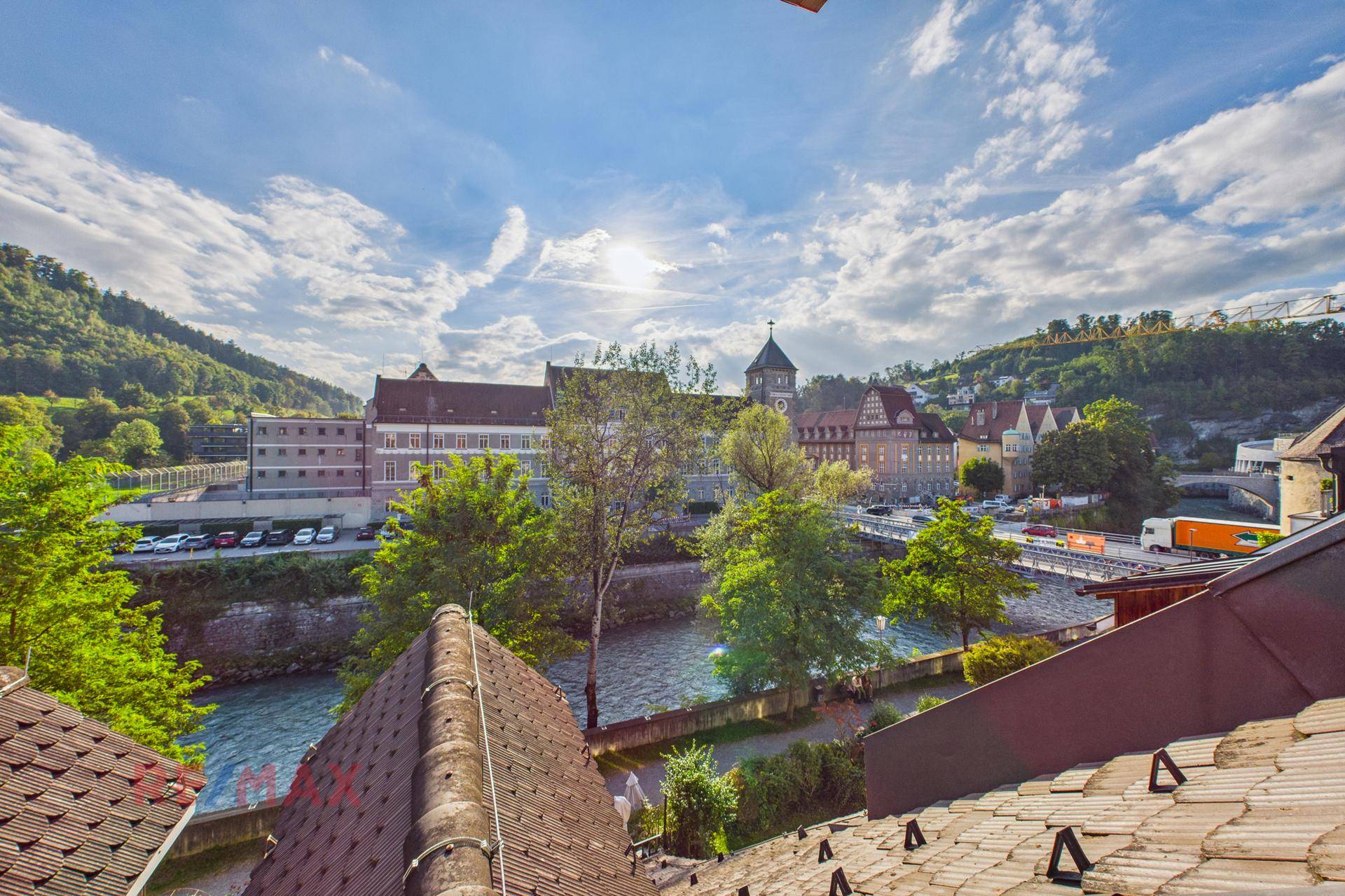 Panoramablick über die Stadt mit Fluss, historischen Gebäuden und grünen Hügeln unter blauem Himmel.