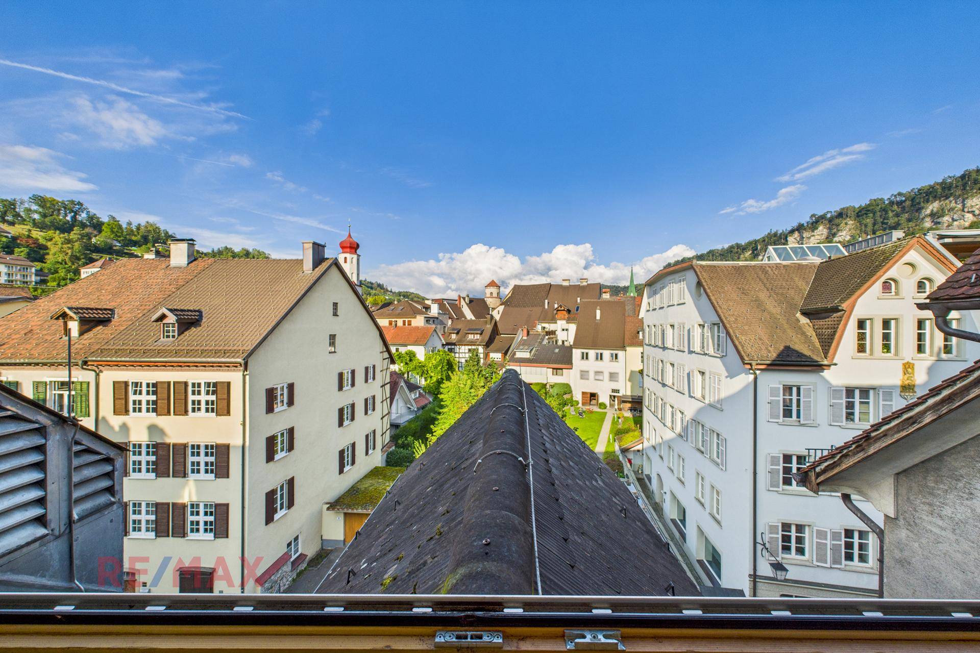 Weitblick über die Dächer der Altstadt mit traditionellen Gebäuden und einem Kirchturm unter blauem Himmel.