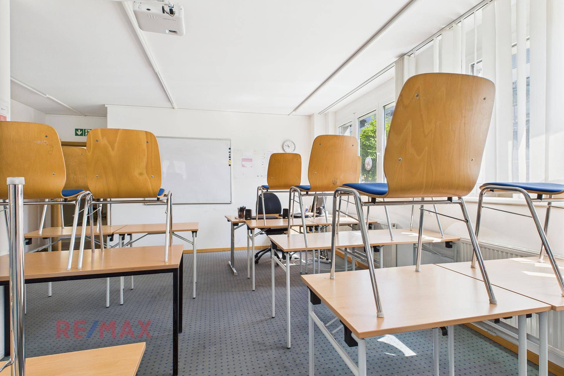 Klassenzimmer mit aufgestellten Tischen und Stühlen, einer weißen Tafel und einem Projektor.