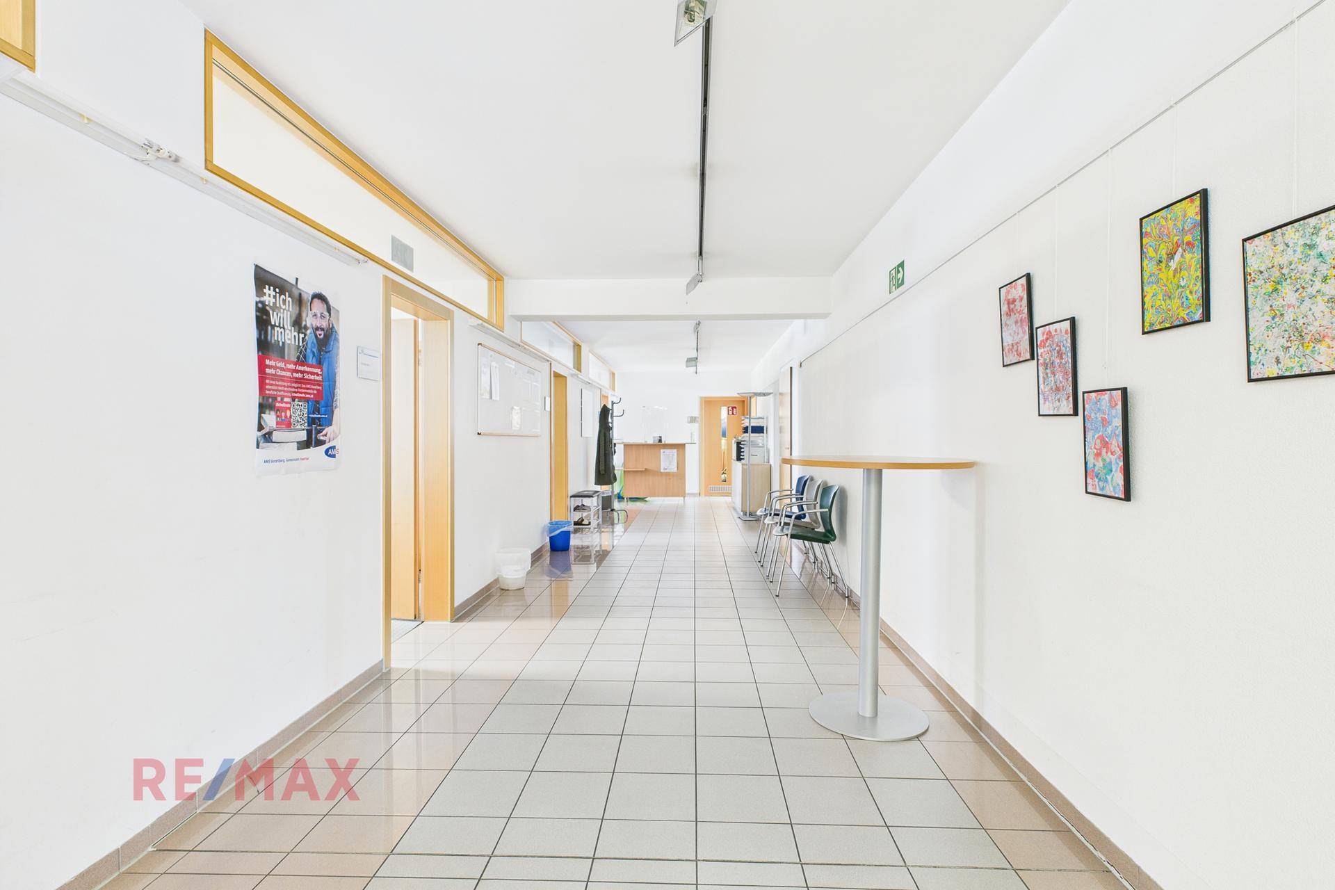 Heller Flur mit Fliesenboden und Kunstwerken an der Wand, der zu verschiedenen Büroräumen führt.