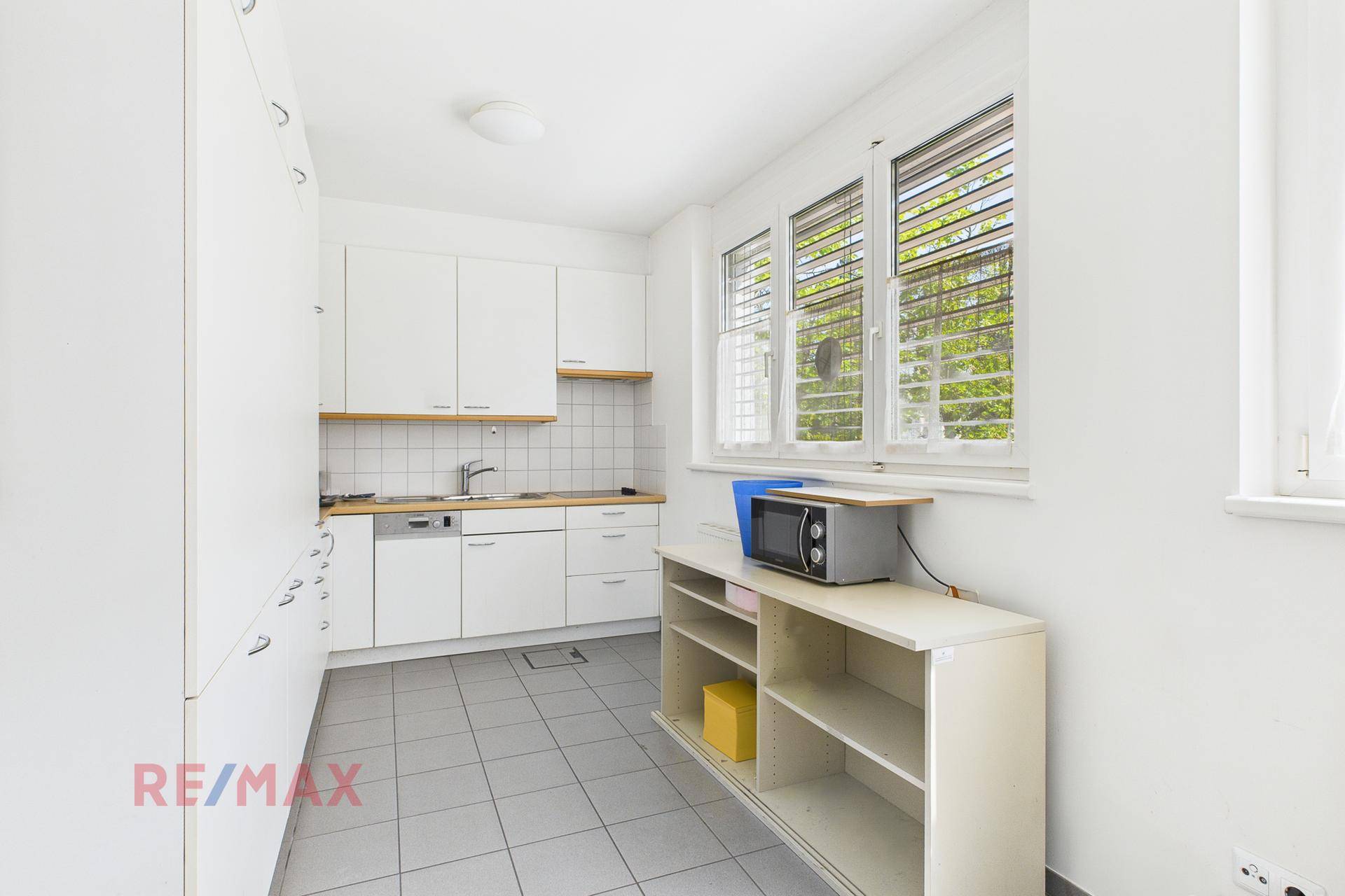 Funktionale Küche mit weißen Schränken, Holztheke und Fenster, ausgestattet mit Mikrowelle und Spüle.