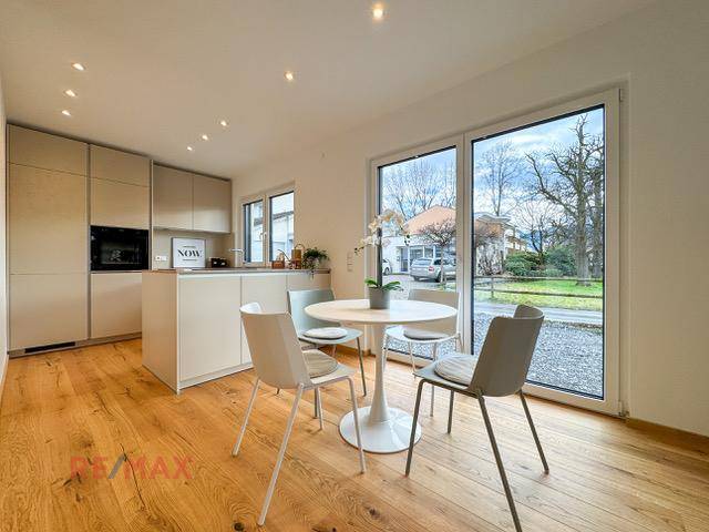 Helle, moderne Küche mit Holzboden, integrierten Geräten und Essbereich am Fenster.