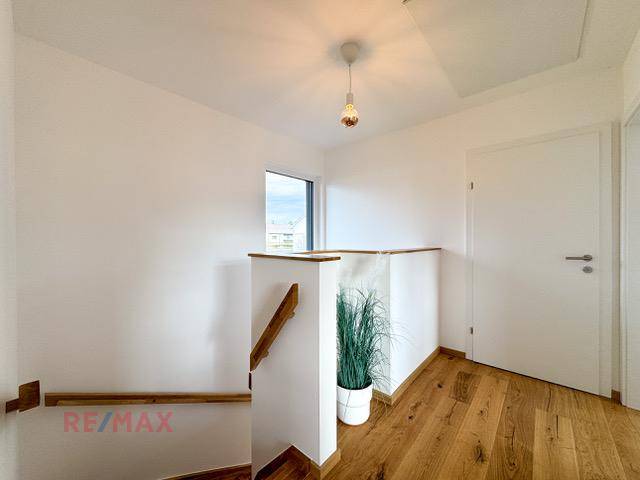 Heller Flur mit Holztreppe und Fenster, das Tageslicht hereinlässt, freundlich und offen.