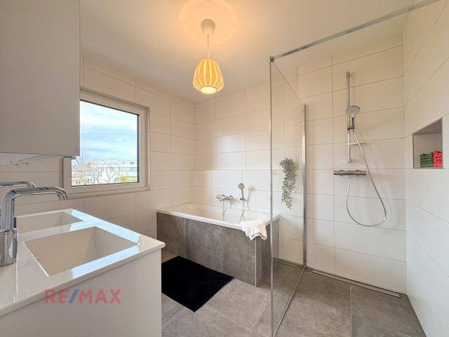 Modernes Badezimmer mit Badewanne, ebenerdiger Dusche und Doppelwaschbecken, hell gefliest.