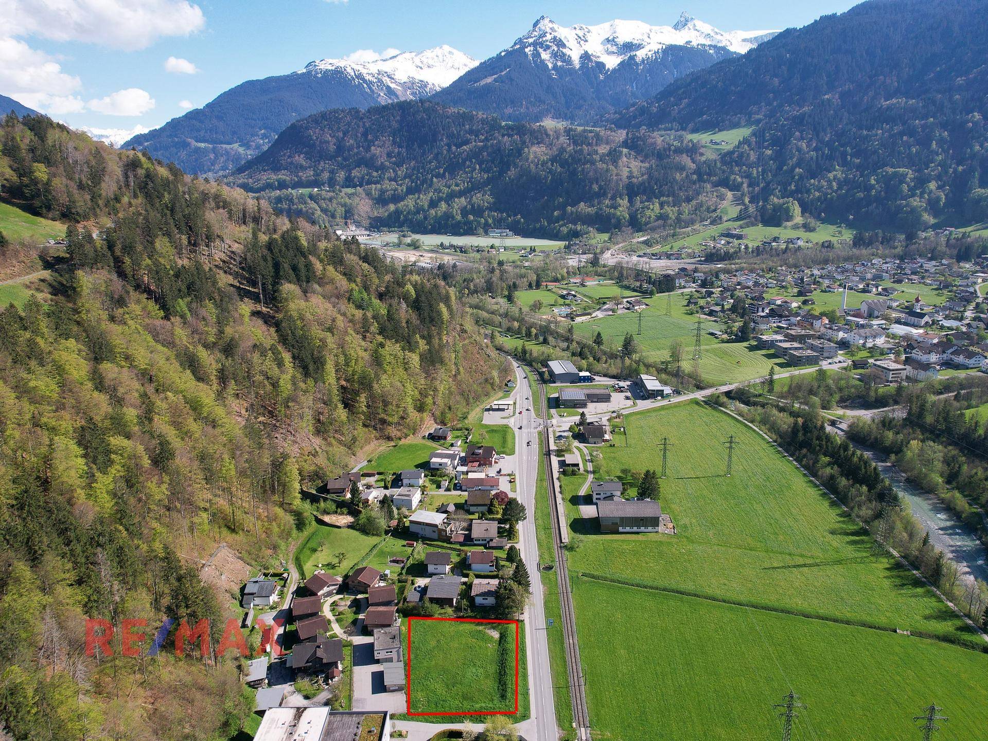 Weitläufige Luftaufnahme eines Tals mit Bergen, Feldern und Siedlungen unter blauem Himmel.