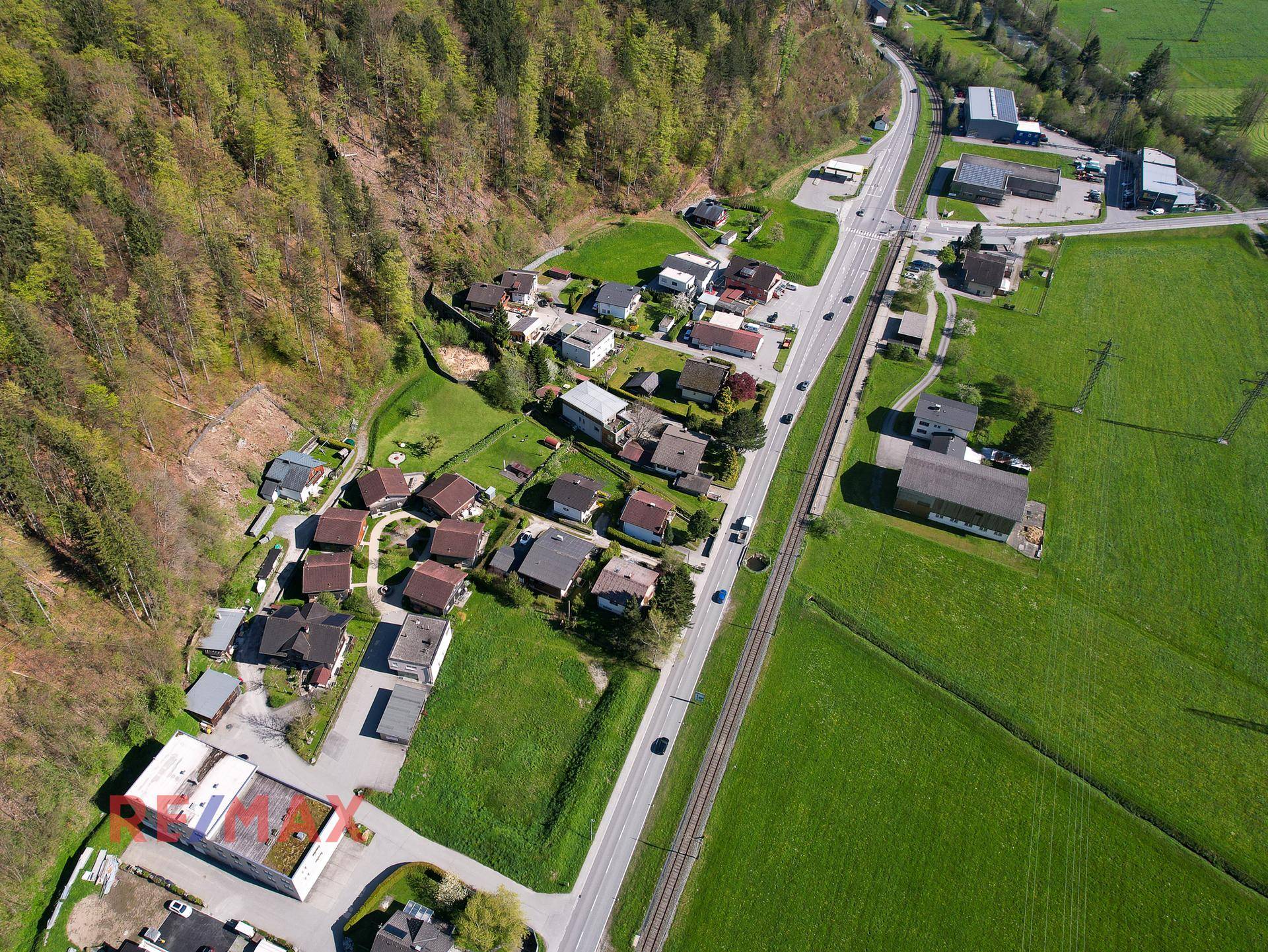 Luftaufnahme einer ländlichen Siedlung mit Häusern, Straße und Feldern, umgeben von Natur.