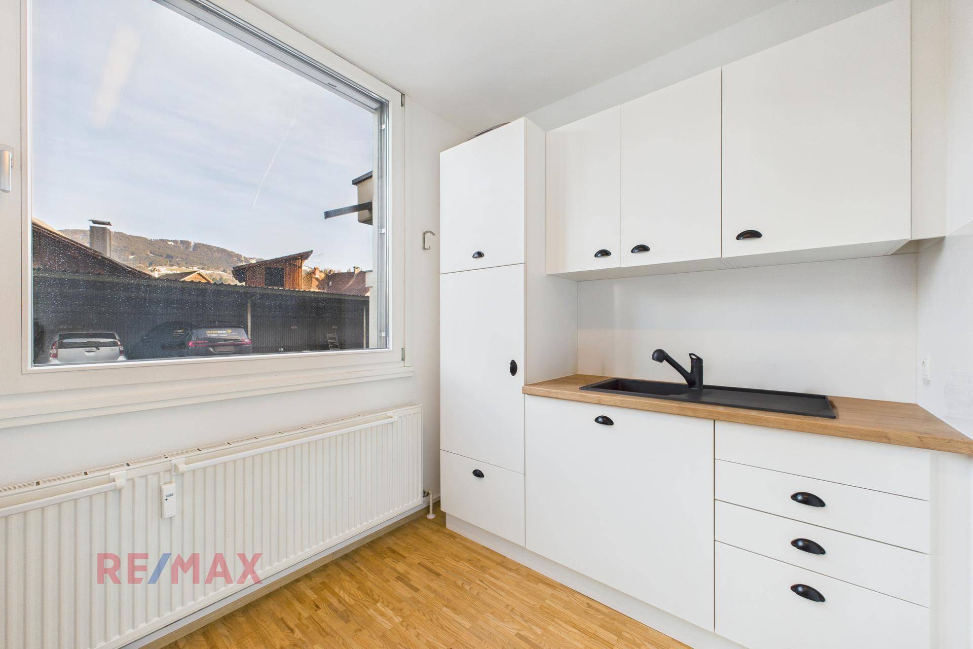 Kleine, funktionale Küchenzeile mit weißen Schränken, Holztheke und Fensterblick.