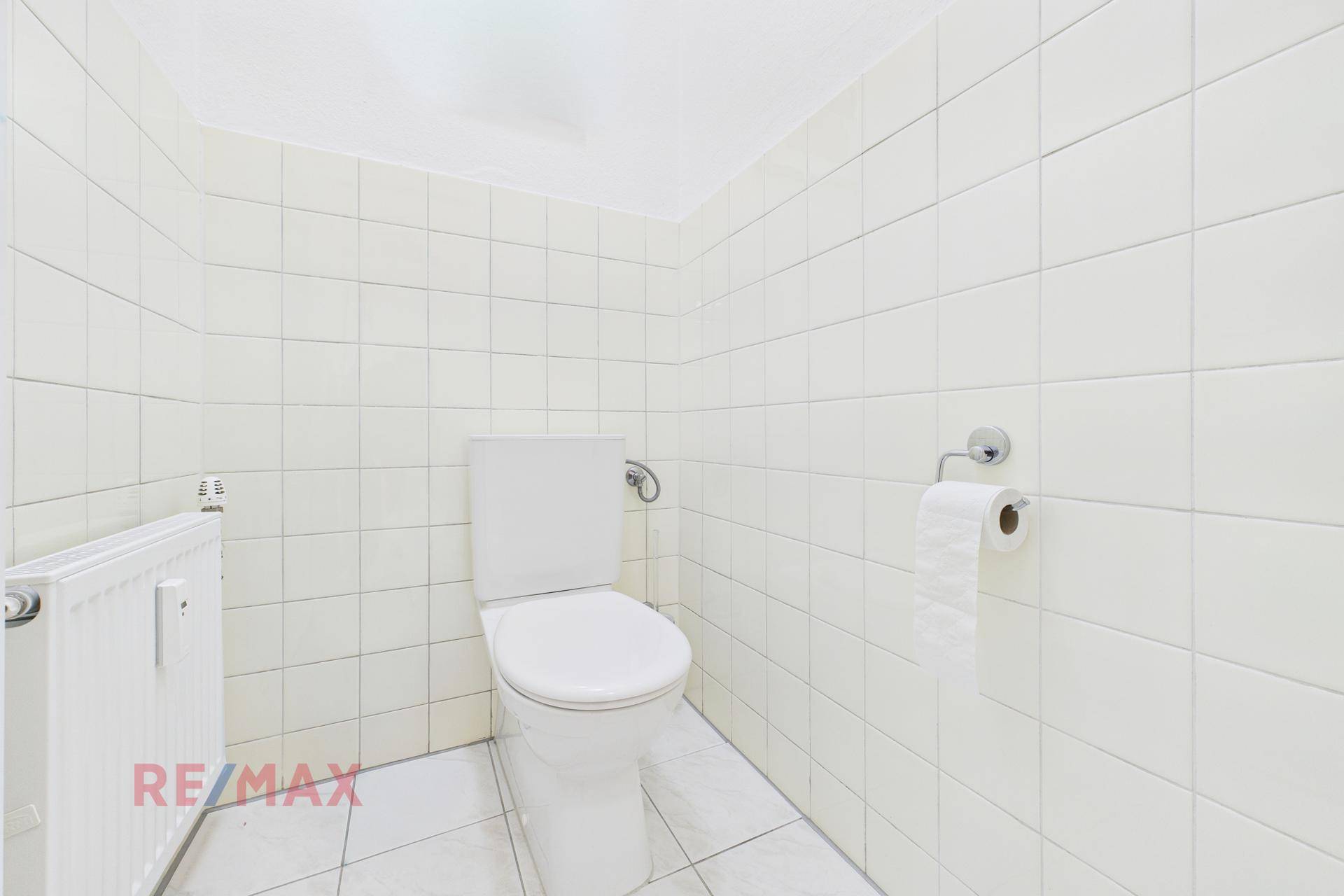 Separate Toilette mit weißen Fliesen an Wänden und Boden, sowie Heizkörper.
