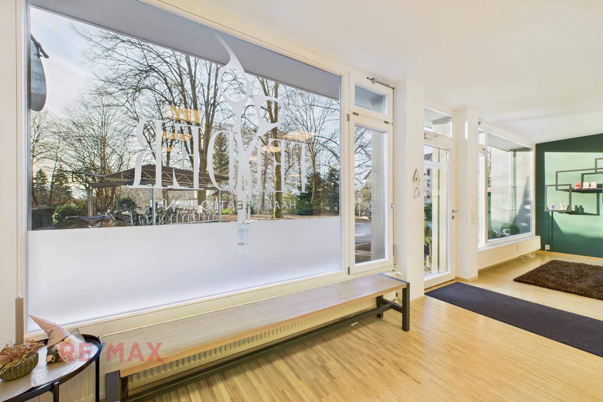 Eingangsbereich des Salons mit großer Fensterfront, Sitzbank und Blick auf die grüne Umgebung.