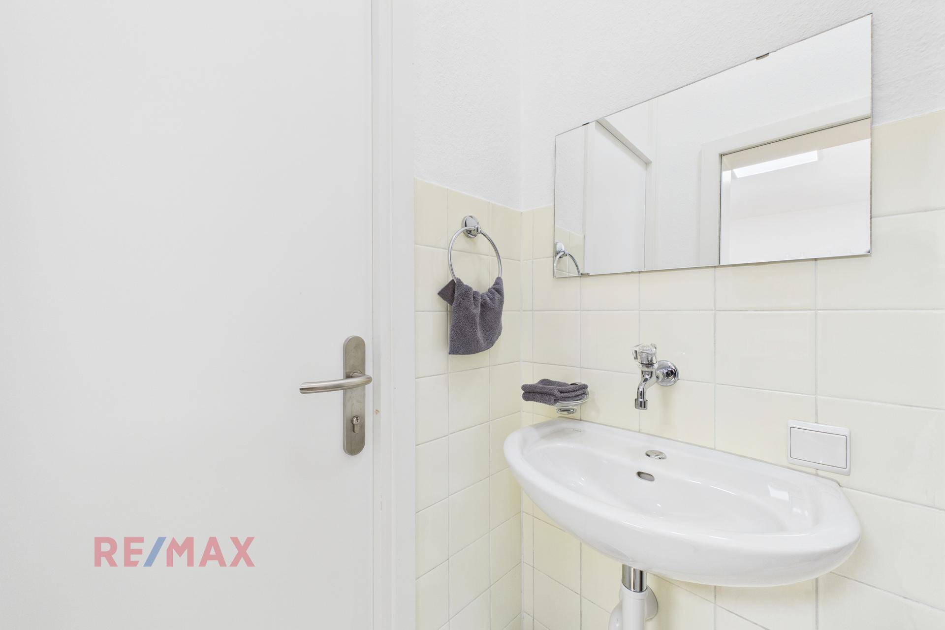 Kleines Gäste-WC mit Waschbecken, Spiegel und hellen Fliesen an den Wänden.
