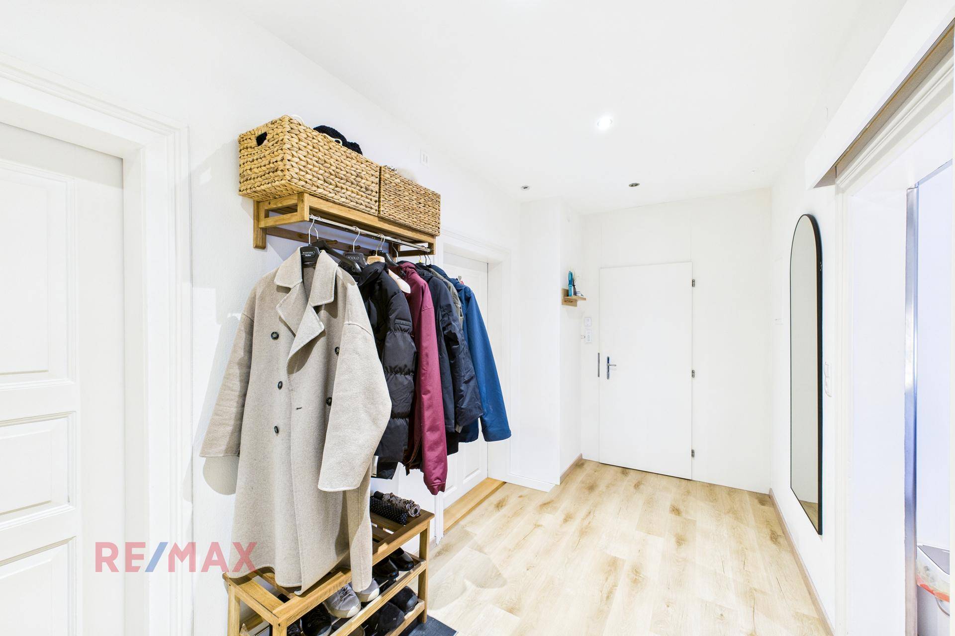 Heller Flur mit Holzfußboden, Garderobe und Spiegel, der zu weiteren Räumen führt.