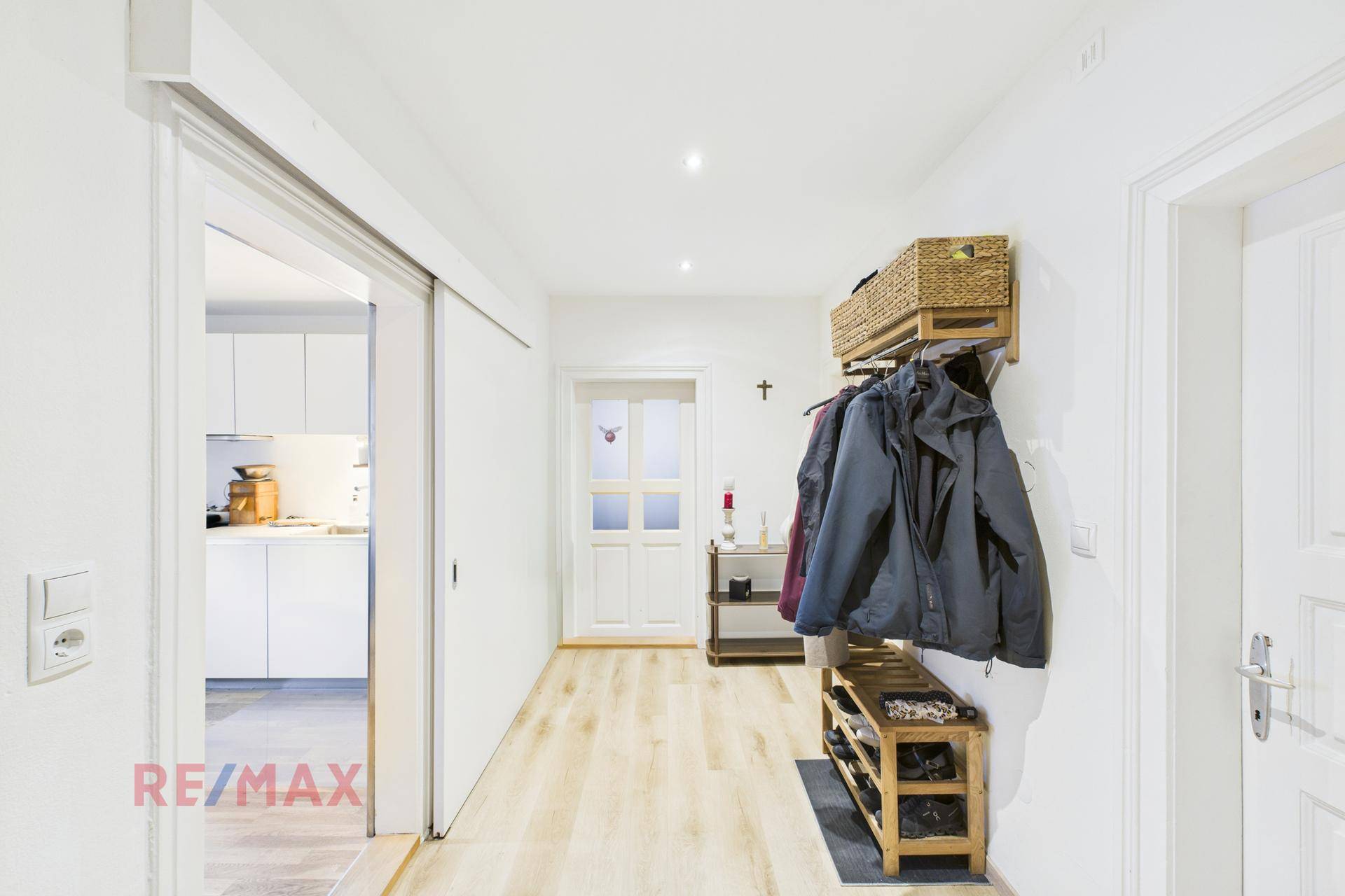 Flur mit Schiebetür, Holzfußboden und Garderobe, der den Blick in die Küche freigibt.