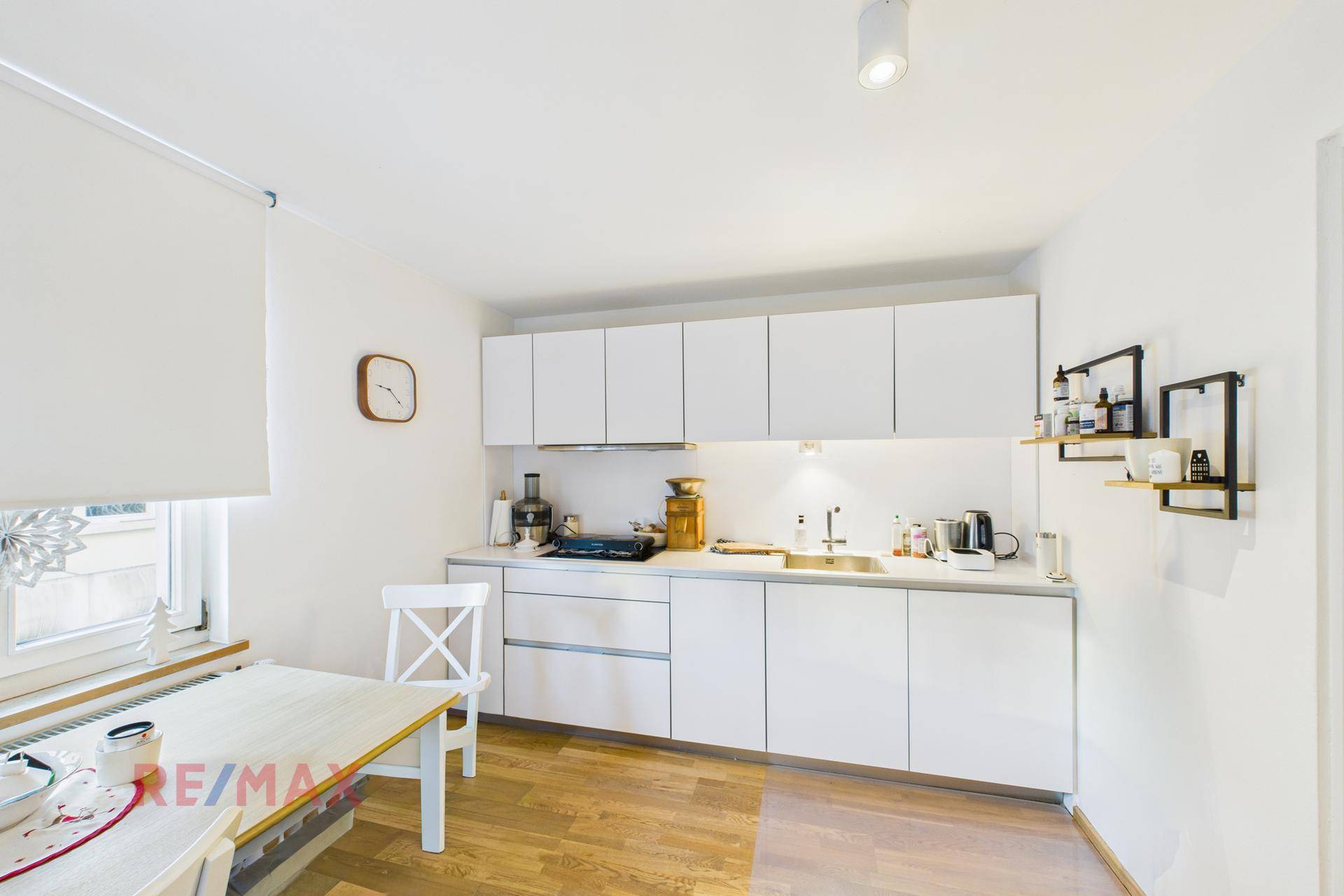 Moderne weiße Einbauküche mit Holzarbeitsplatte und Essbereich am Fenster.
