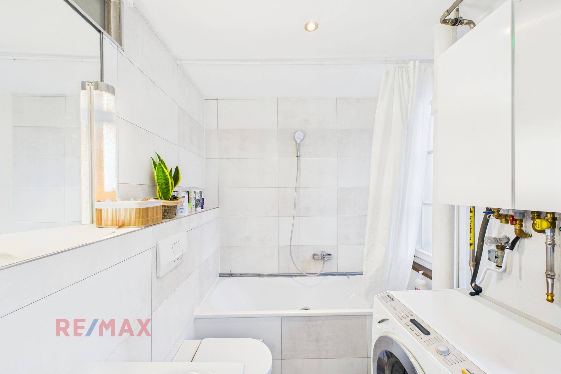 Helles Badezimmer mit Badewanne, Dusche, Waschmaschine und weißen Fliesen.