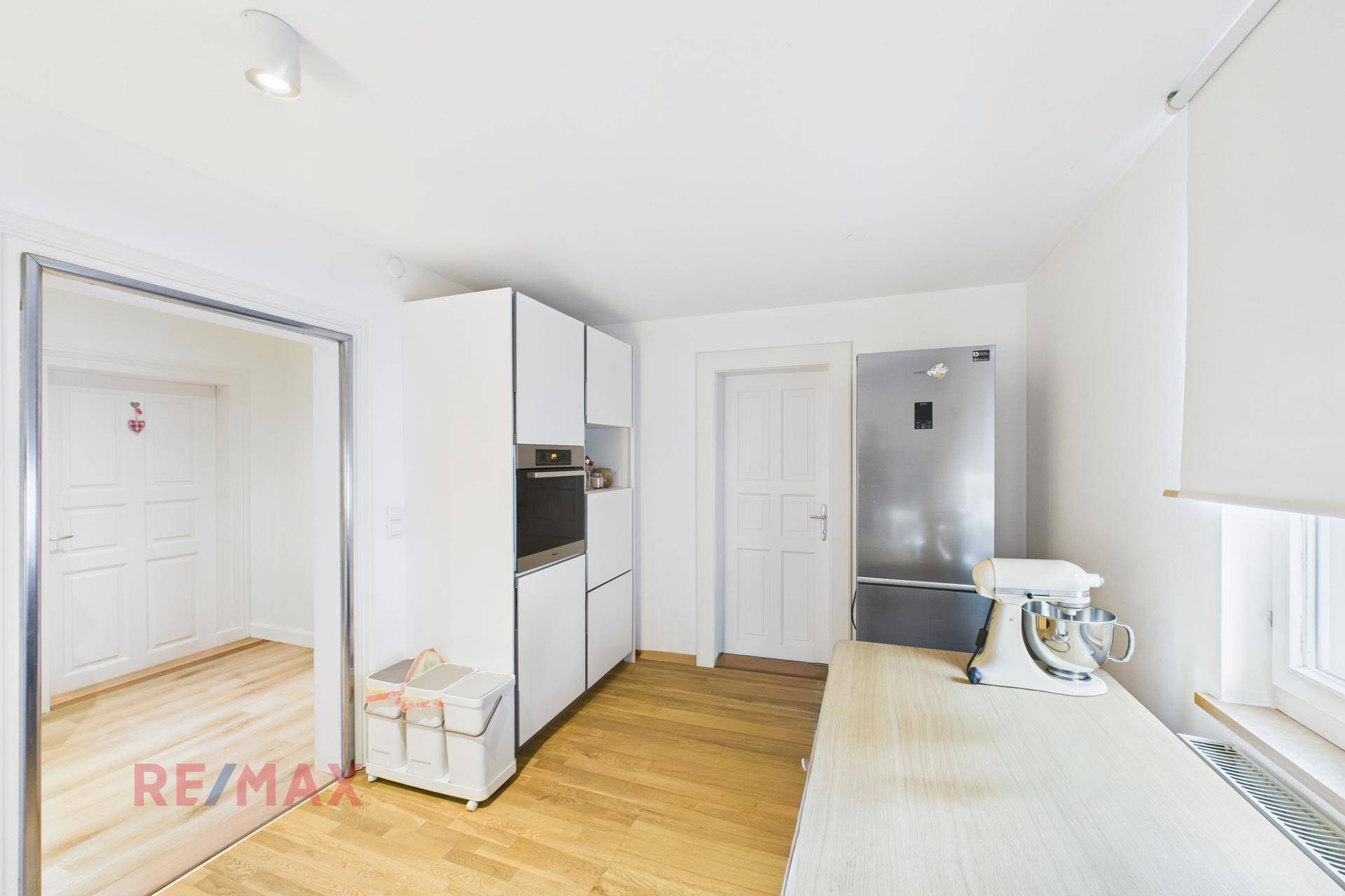 Helle Einbauküche mit weißen Schränken, integriertem Backofen und Kühlschrank.