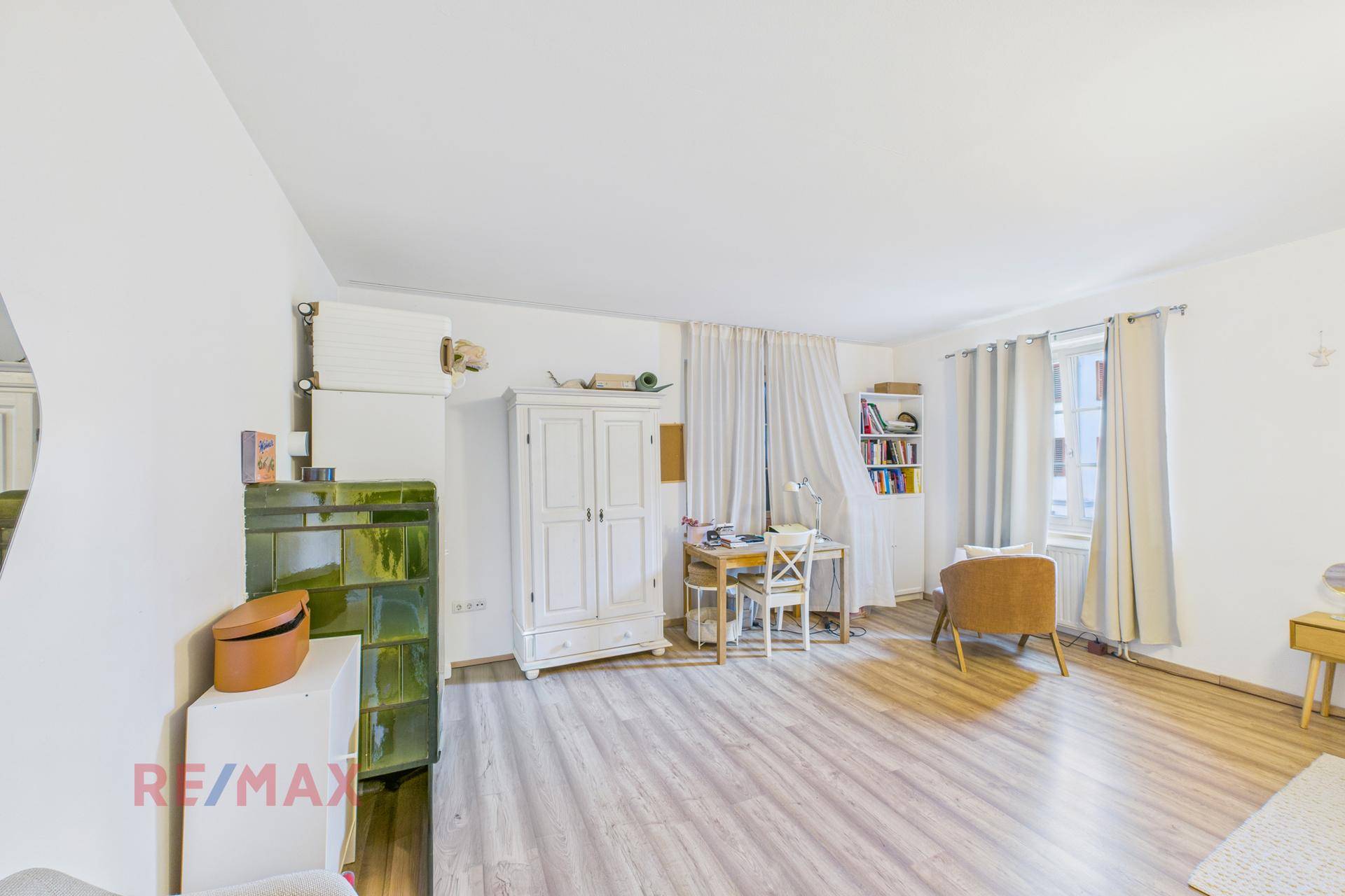 Geräumiges Zimmer mit Kachelofen, Schreibtisch und hellem Laminatboden, vielseitig nutzbar.